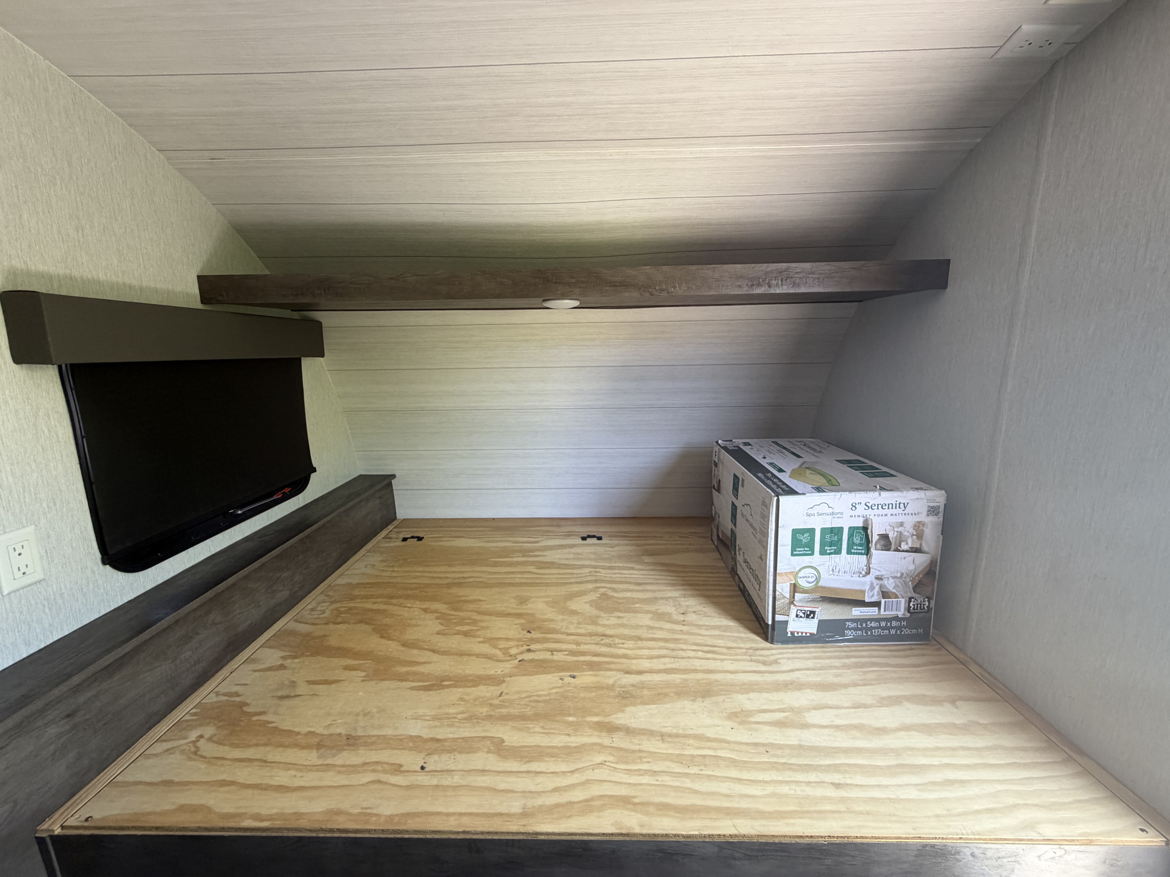 RV rental bedroom: a new boxed mattress sits on the plywood bed base, next to a mounted TV and overhead shelf.. Forest River Salem Select 2021