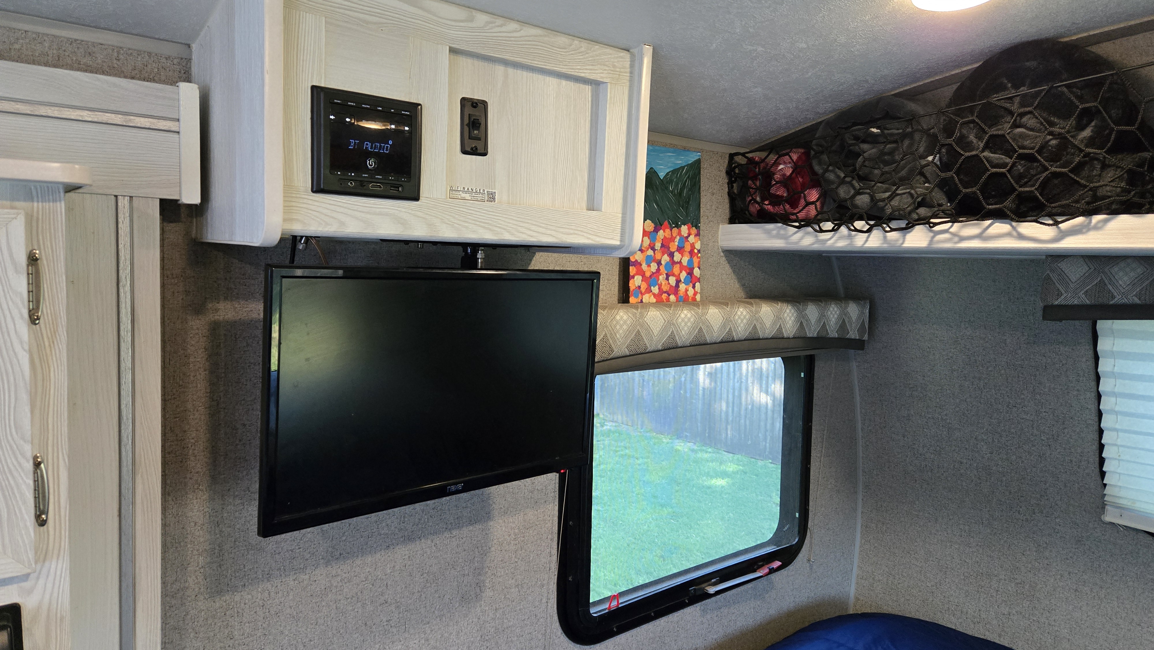 An RV rental interior featuring a mounted TV, overhead stereo, window, and netted bunk storage for a cozy camper experience.. Forest River Flagstaff E-Pro 2021