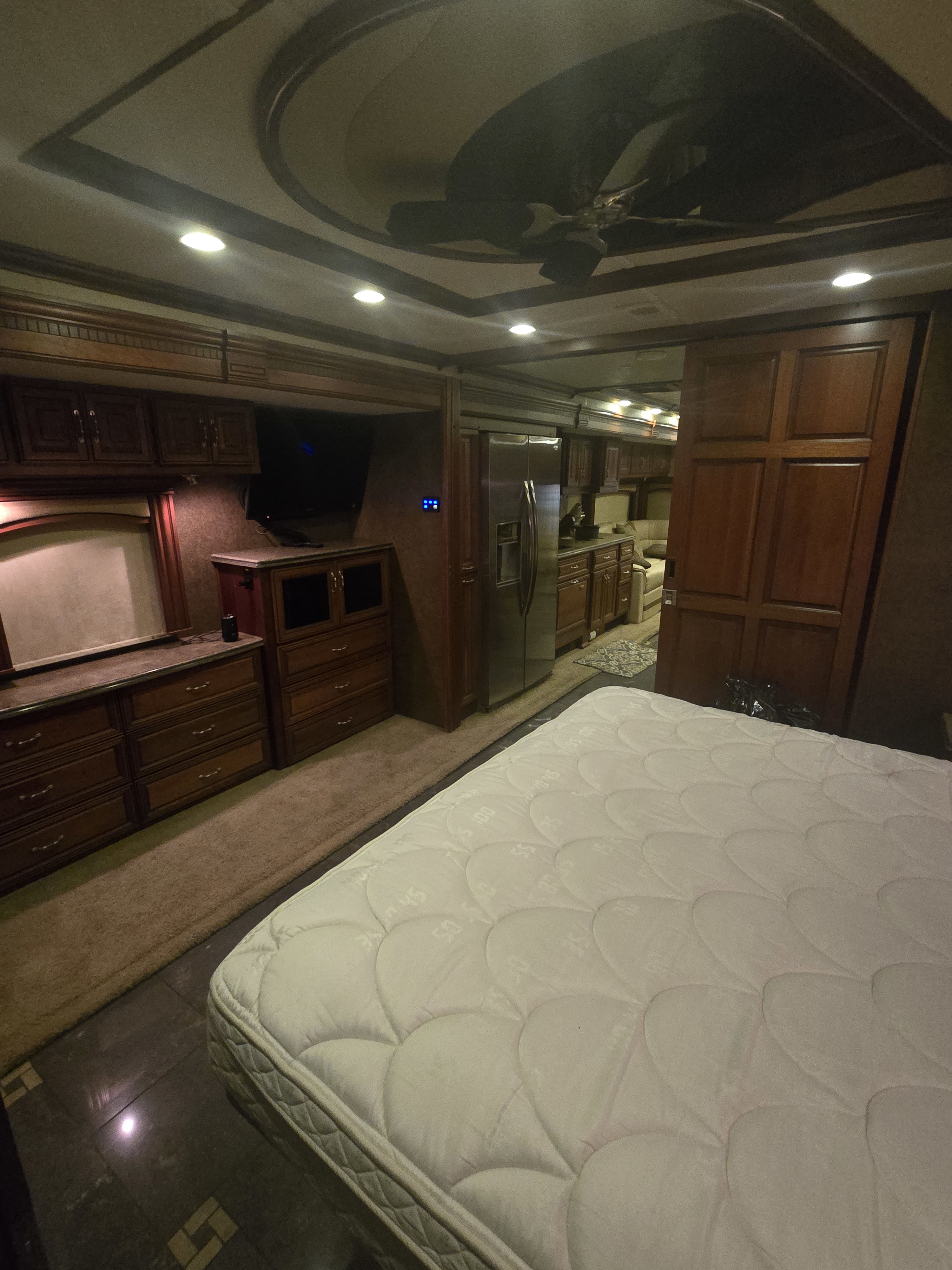 RV rental bedroom featuring a large mattress, wooden cabinets, ceiling fan, and an open view to the kitchen.. American Eagle American Eagle Motorhome 2012