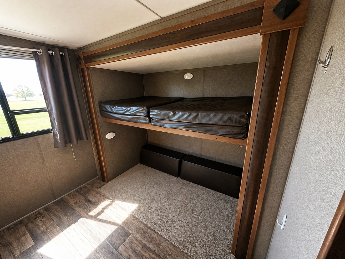 RV rental: Bunk beds inside a camper, featuring dark mattresses, a bright window with curtains, wood trim, and mixed flooring.. Keystone RV Springdale 2017