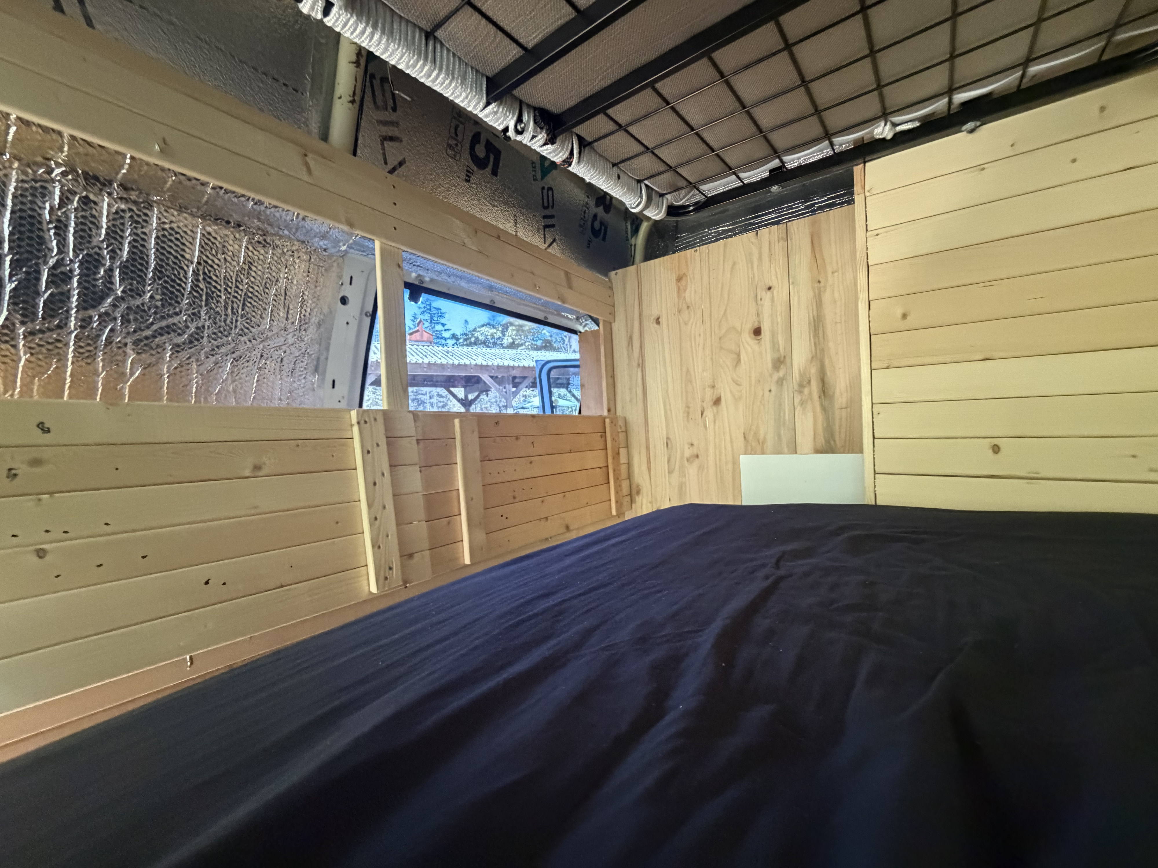 RV rental van conversion interior featuring a cozy bed, wood paneling, insulation, and a window view.. Ford Econoline 150 1992
