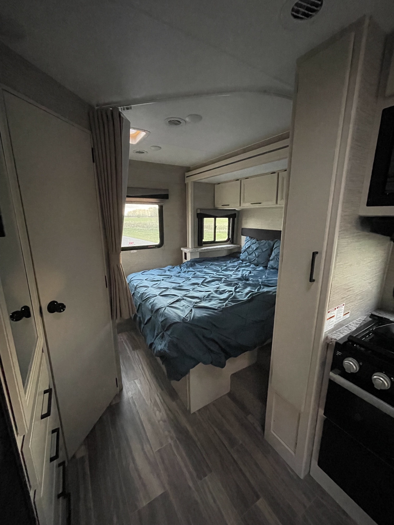 Compact rv rental bedroom: blue bed with pleated cover, light wood-look cabinets, and plank flooring create a cozy interior.. Thor Freedom Elite 2022