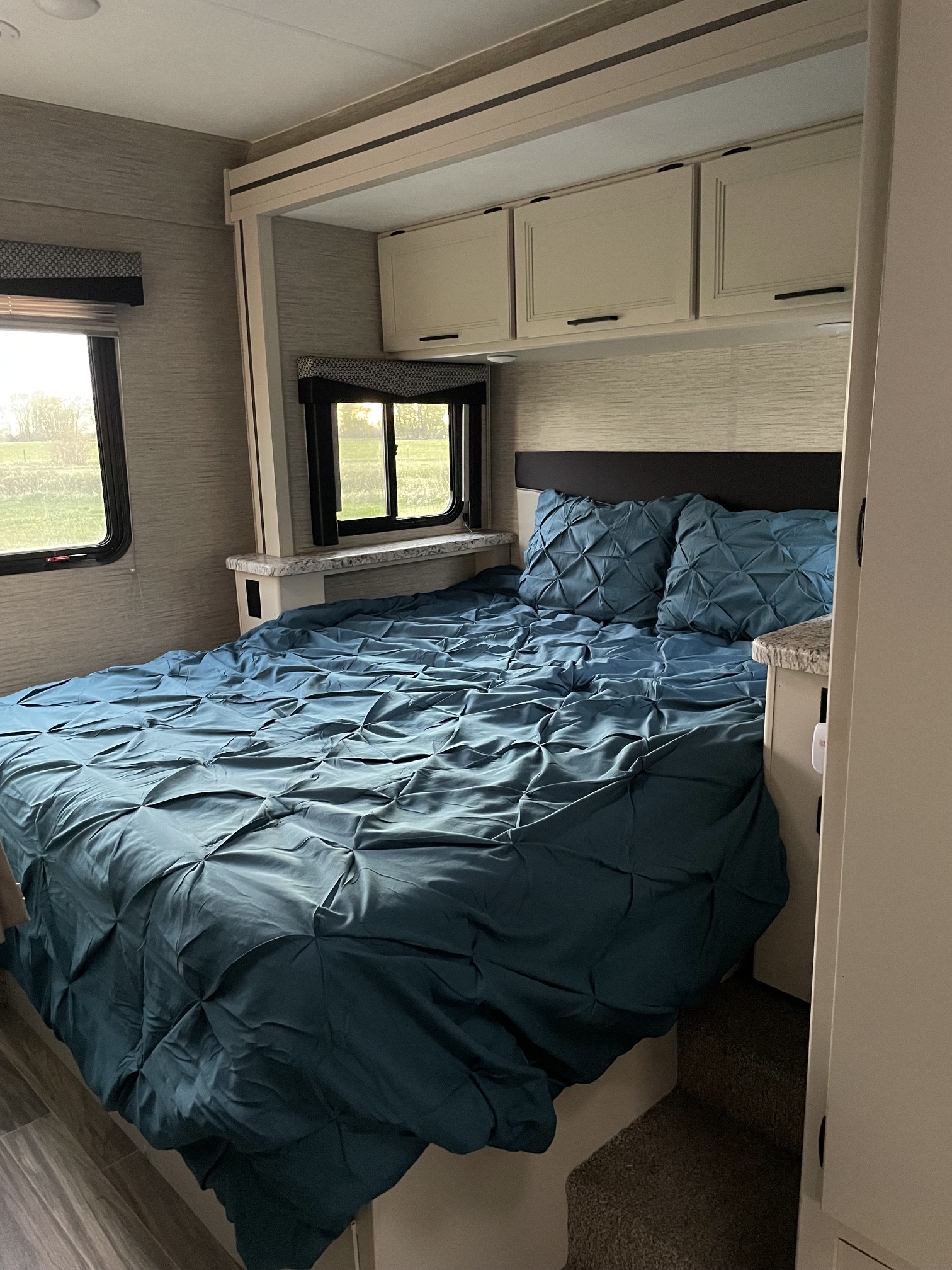Cozy RV rental bedroom with a large bed in blue bedding, two windows, overhead cabinets, and nightstands.. Thor Freedom Elite 2022