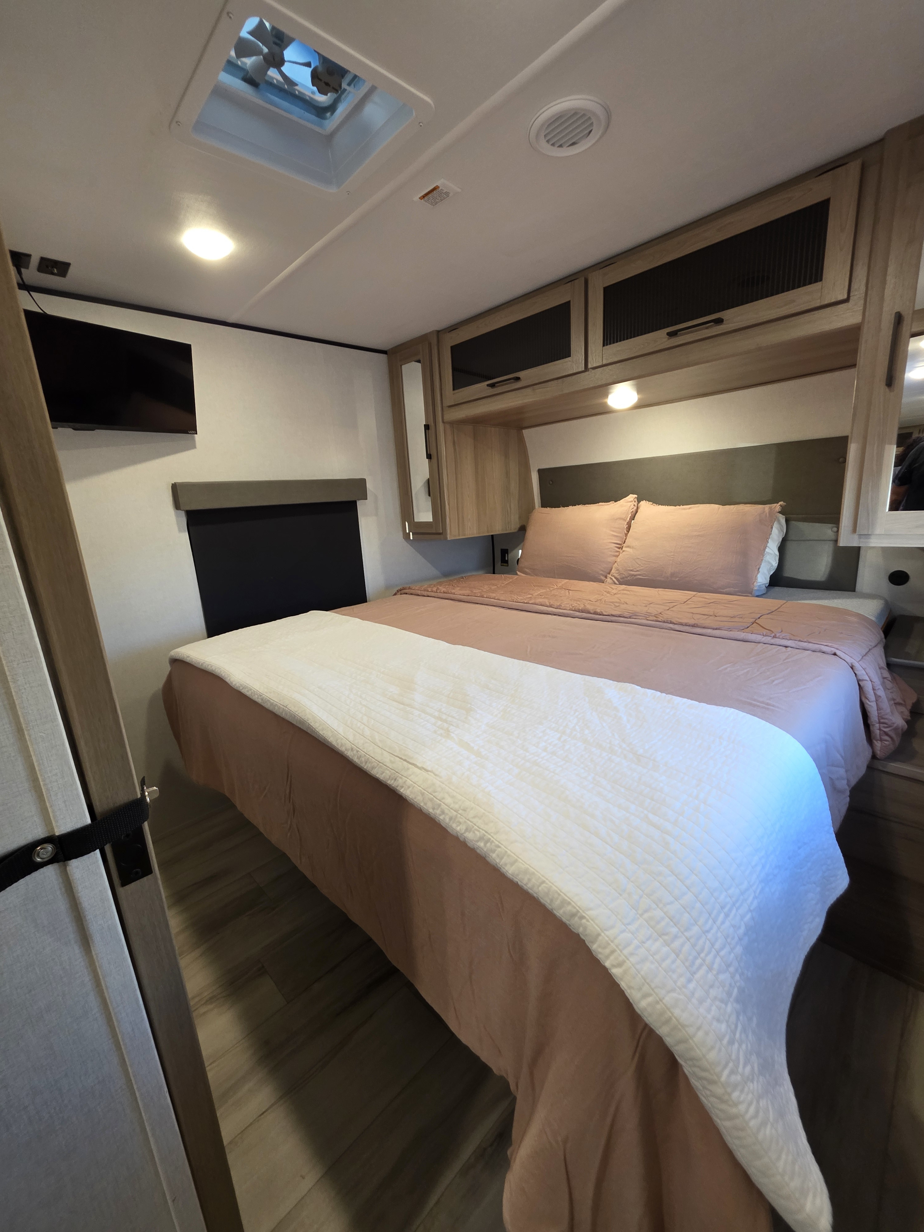 Cozy RV rental bedroom with pink bedding, overhead cabinets, TV, and ceiling vent, offering a comfortable travel space.. Keystone RV Coleman Legacy 2026