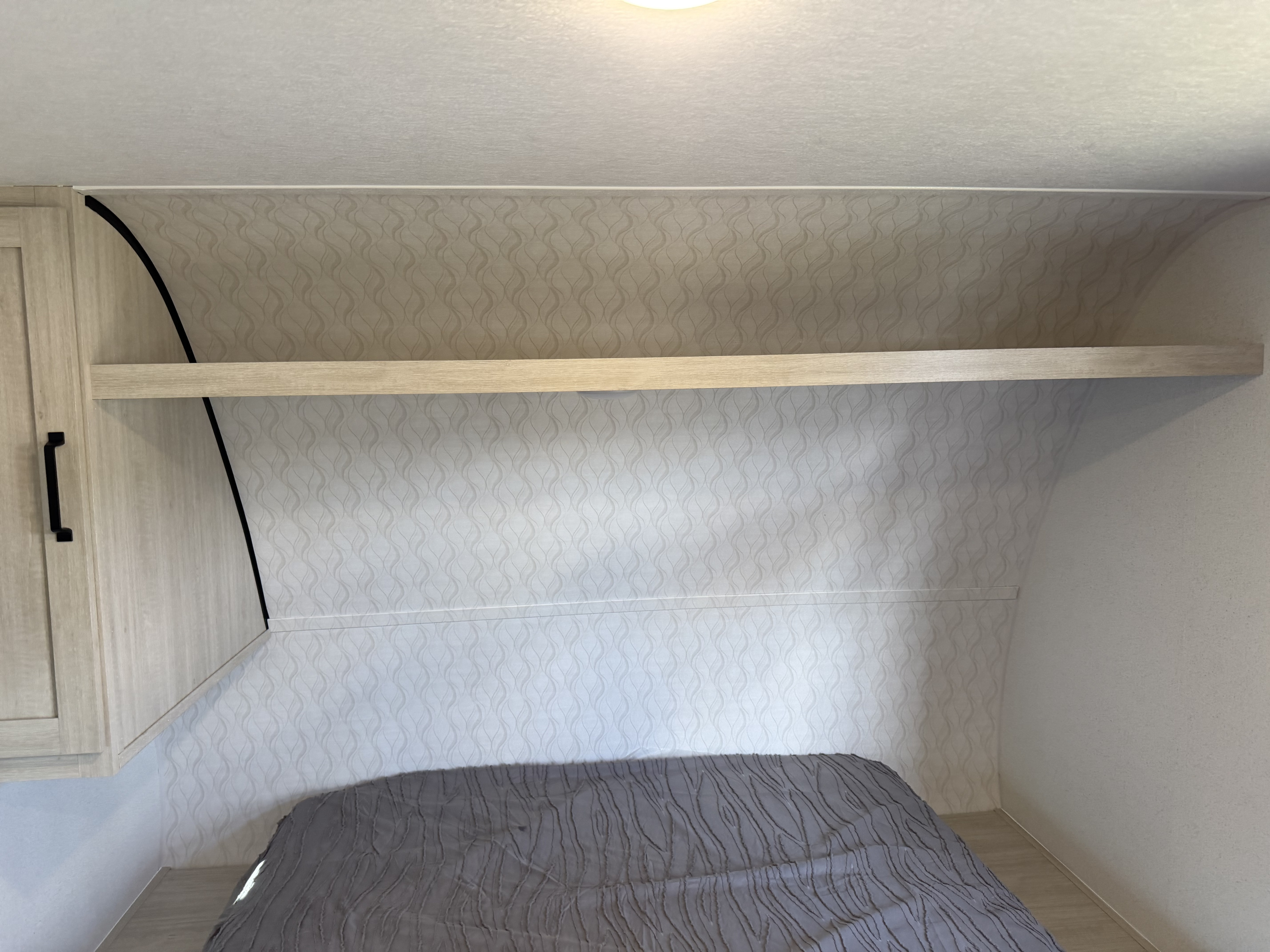 RV rental bedroom with a gray comforter on the bed, a patterned headboard wall, and an overhead shelf next to a cabinet.. Forest River 16dsce 2026