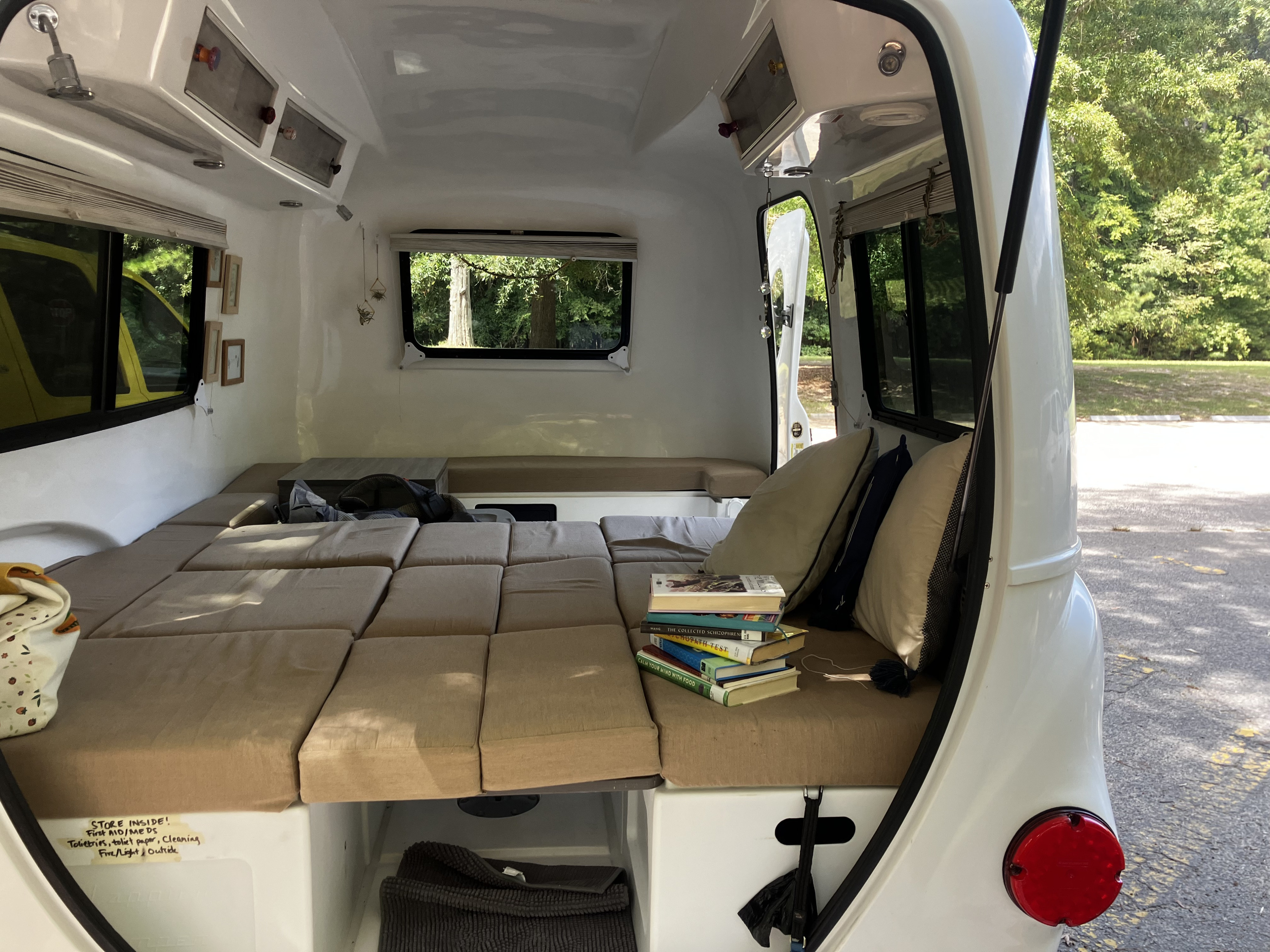 Inside a compact RV rental: a plush bed, stack of books, and smart storage solutions for travelers.. Happier Camper HC1 2022