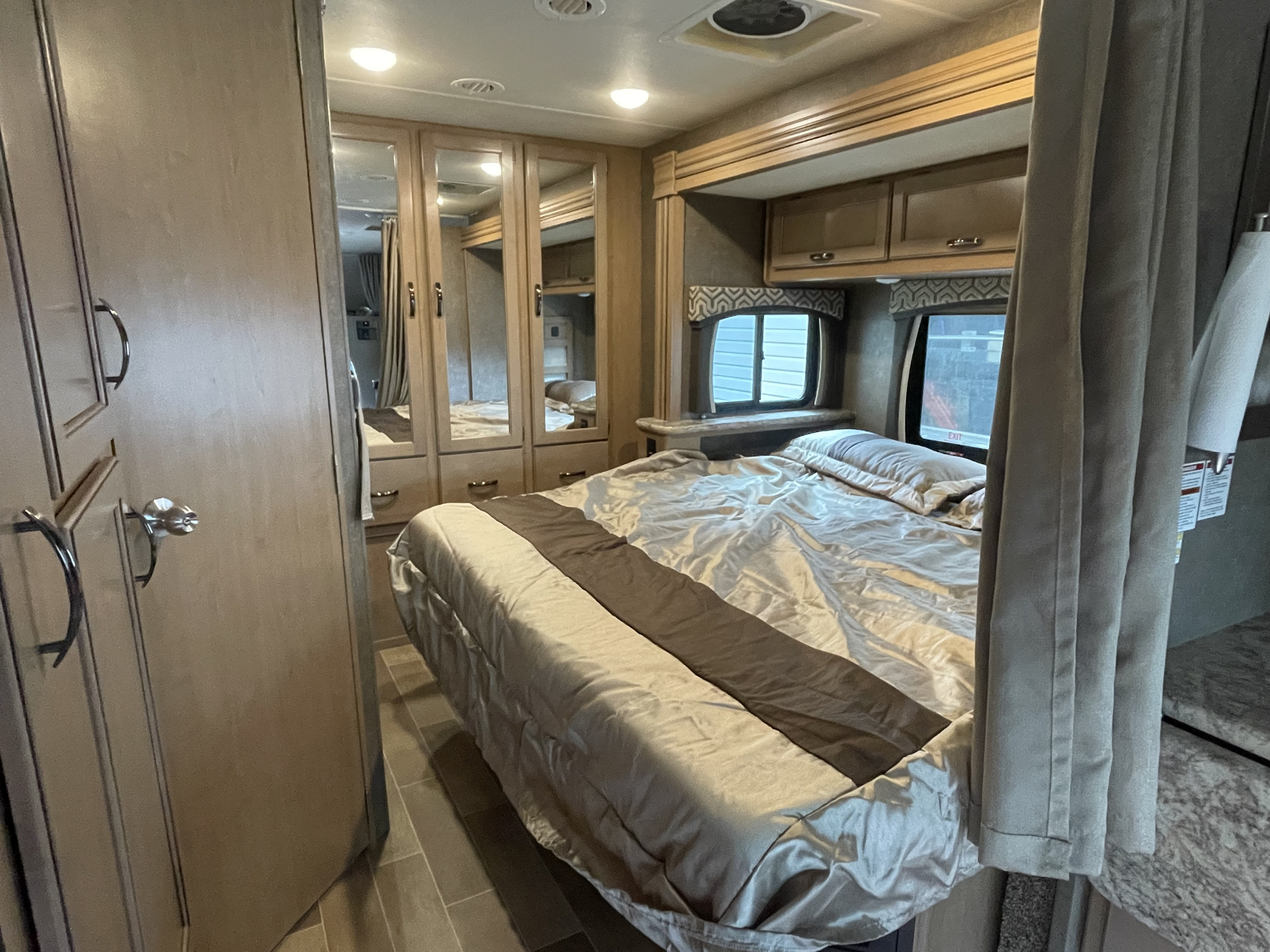 Cozy RV rental bedroom with queen bed, mirrored wardrobe, overhead cabinets, and windows, ready for your next adventure.. Thor Chateau 2020