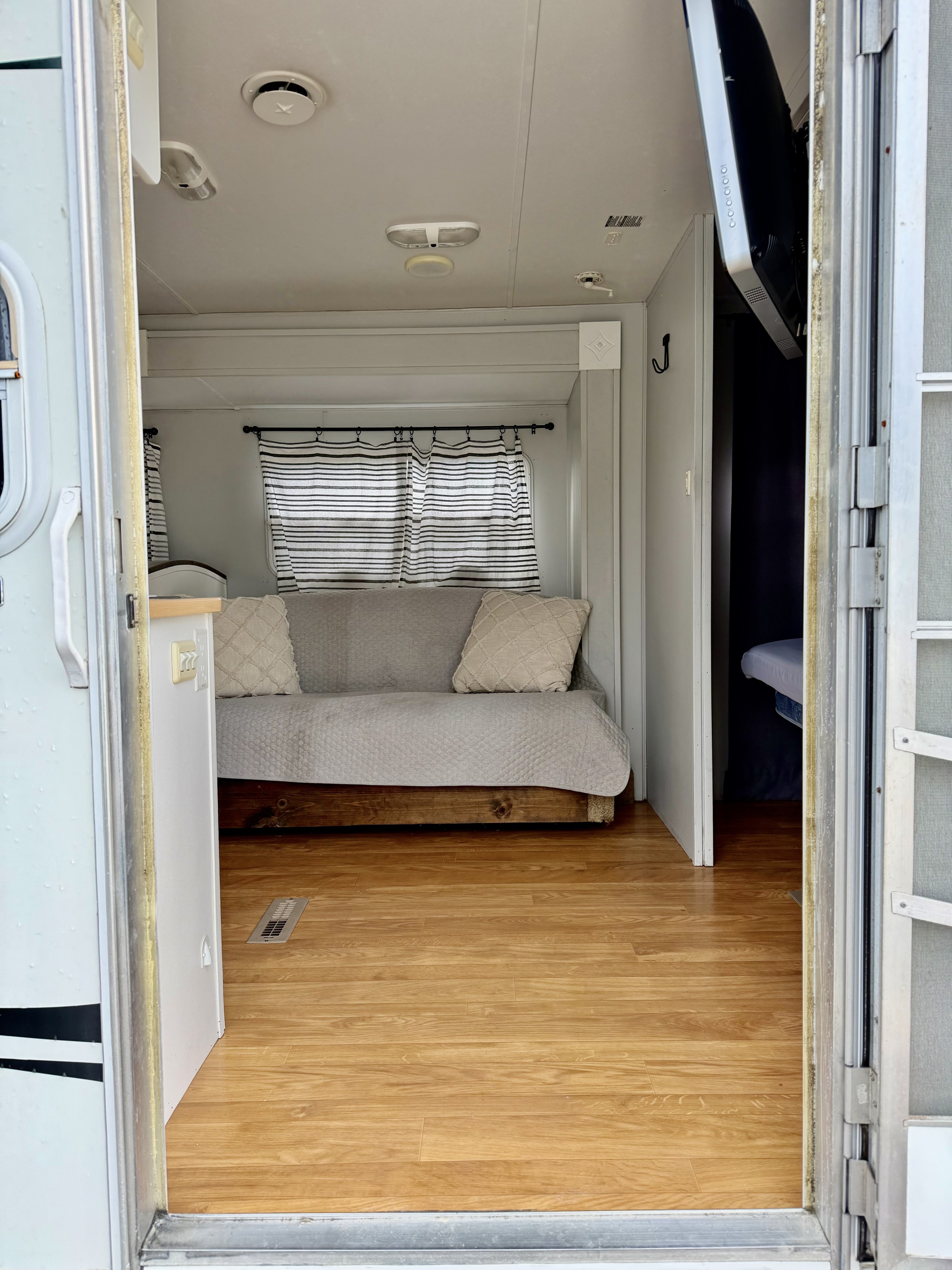RV rental interior: A cozy living space with a light gray sofa, striped curtains, and a light wooden floor.. Starcraft Aruba Tahiti 2005