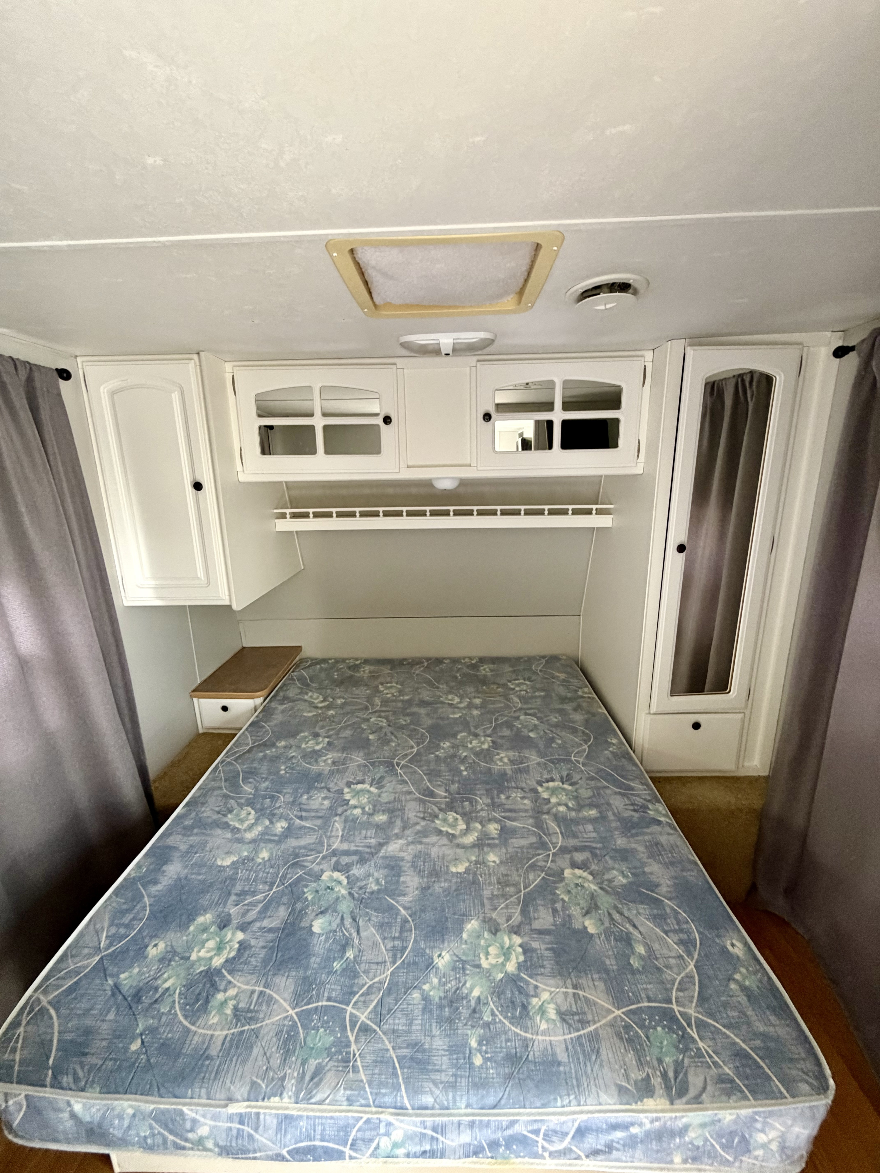 Cozy RV rental bedroom interior with a blue floral mattress, white overhead cabinets, built-in storage, and gray curtains.. Starcraft Aruba Tahiti 2005