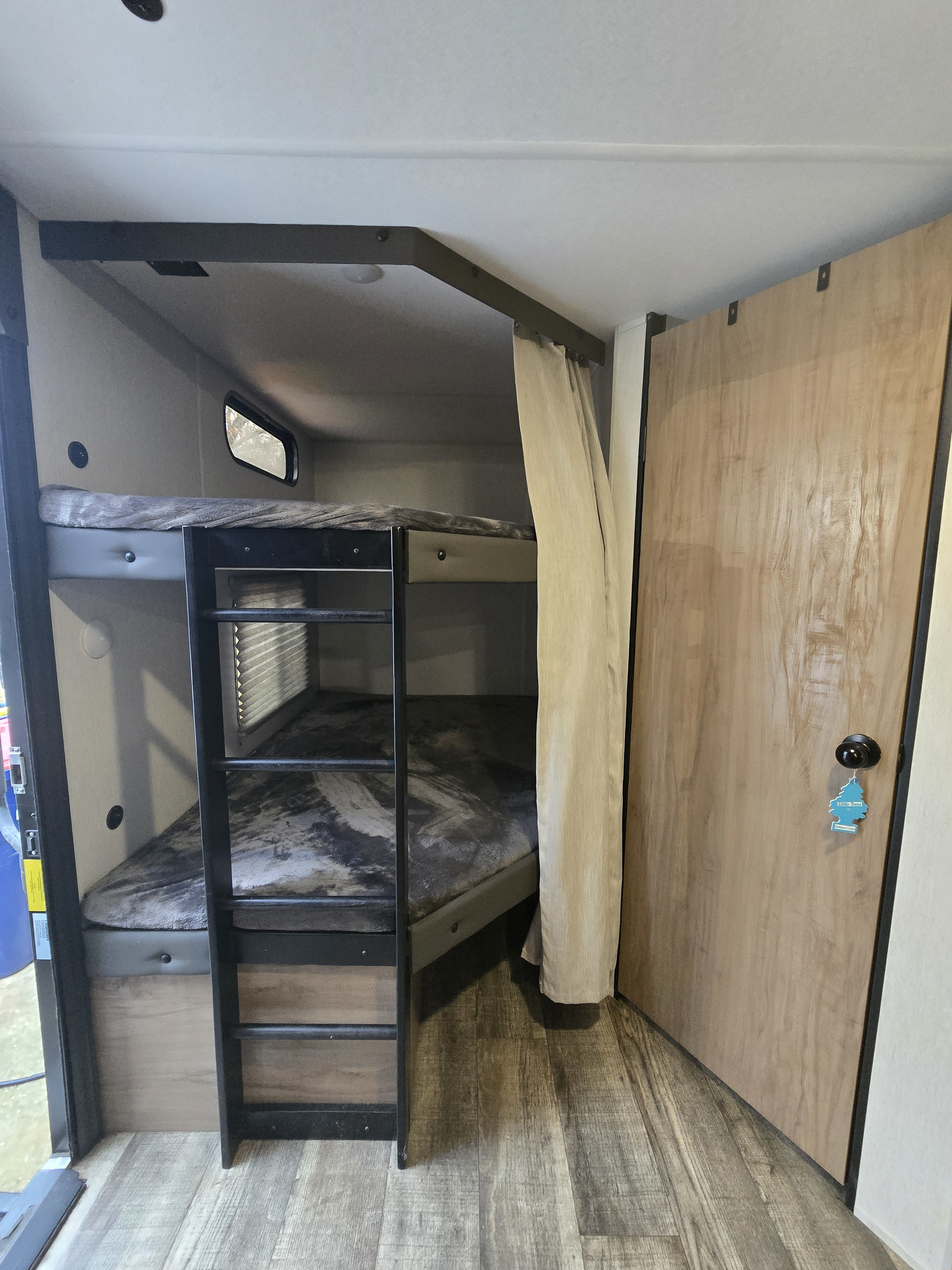 RV rental bunk bed interior with a ladder, privacy curtain, small window, and a light wood door.. Forest River Cherokee Grey Wolf 2024