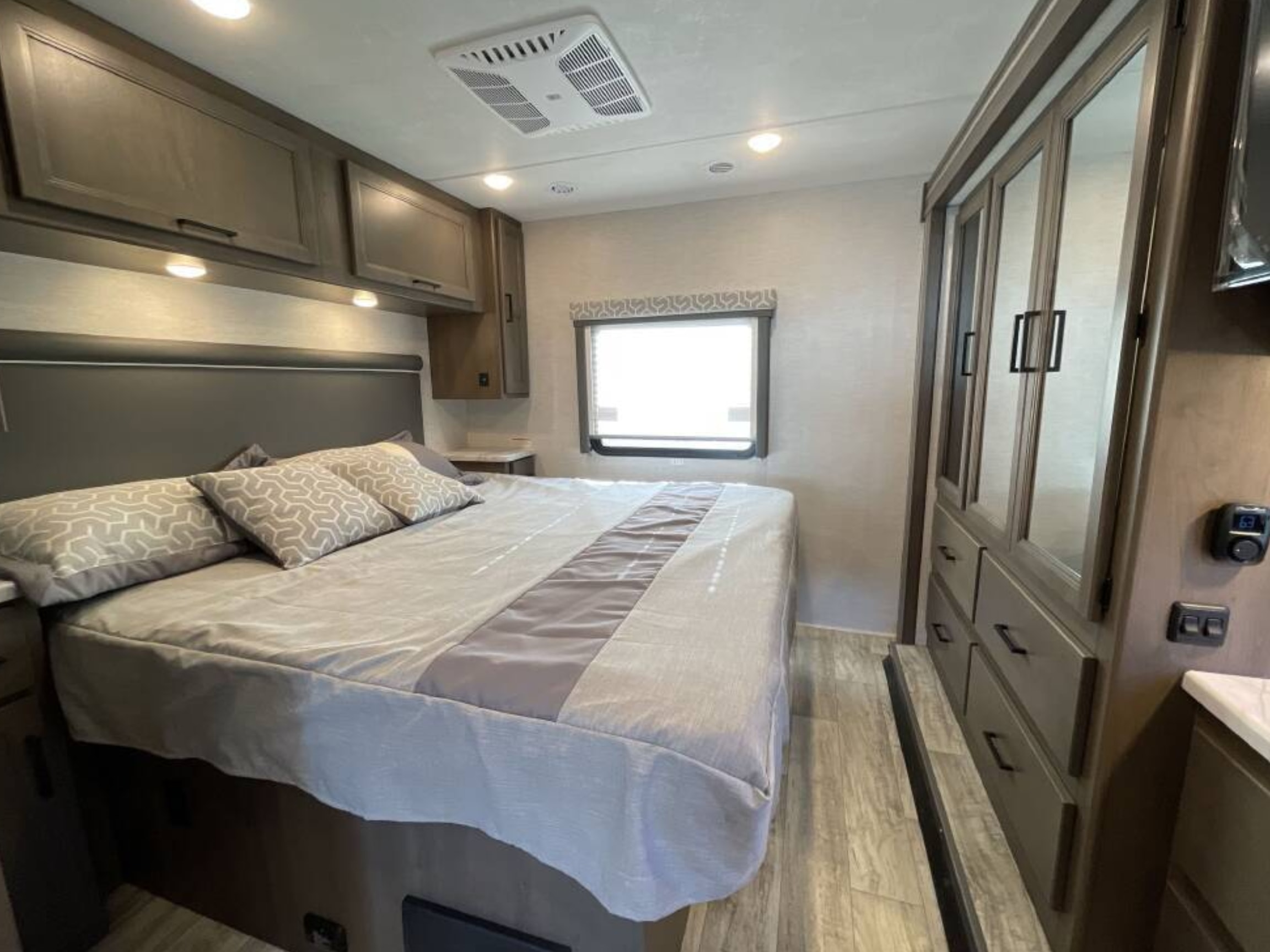 Comfortable RV rental bedroom with a cozy bed, overhead cabinets, and mirrored wardrobe, ideal for your next road trip.. Classe A 31 pieds avec extensions 2024