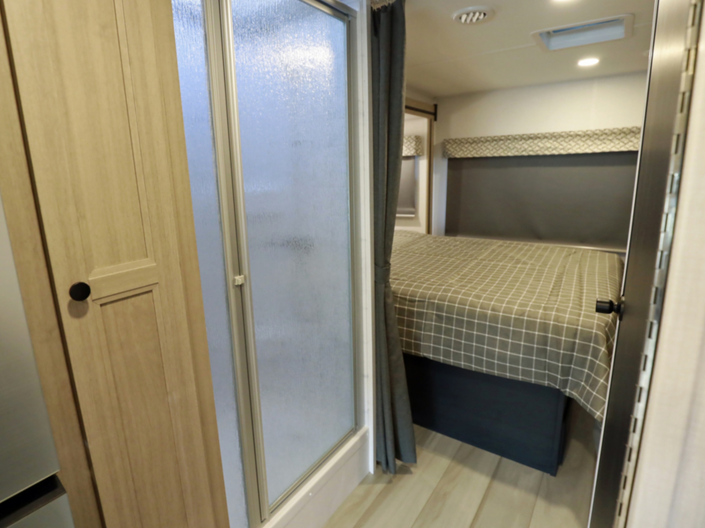 Compact RV rental interior featuring a wooden door, frosted shower, and cozy bedroom with a checkered bedspread.. Classe C C31 pieds avec extension(s) 2023