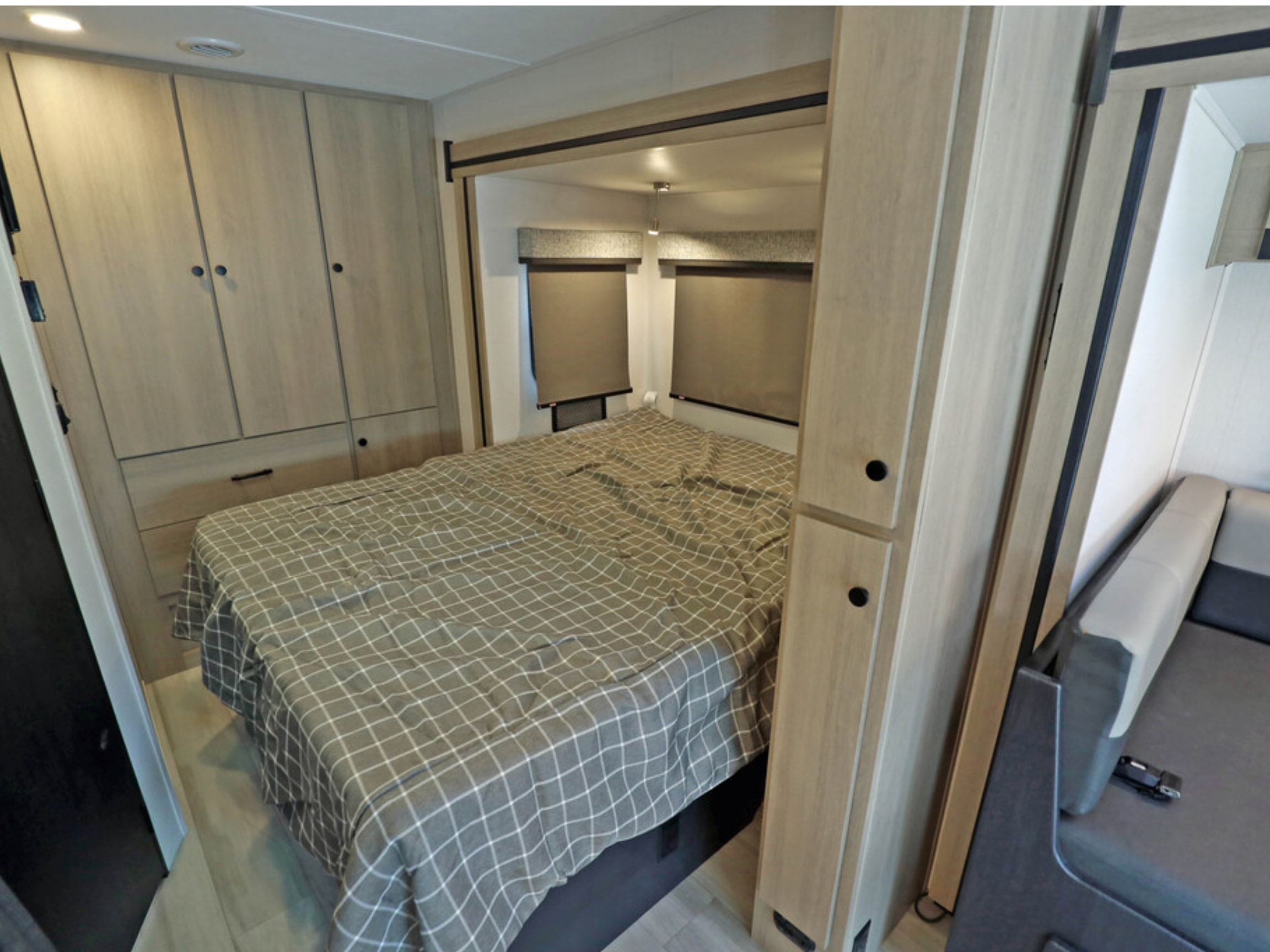 Cozy RV rental bedroom with a comfortable bed, gray plaid spread, light wood cabinets, and pull-down window shades for a restful sleep.. Classe C mercedes 24 pieds avec extension 2021
