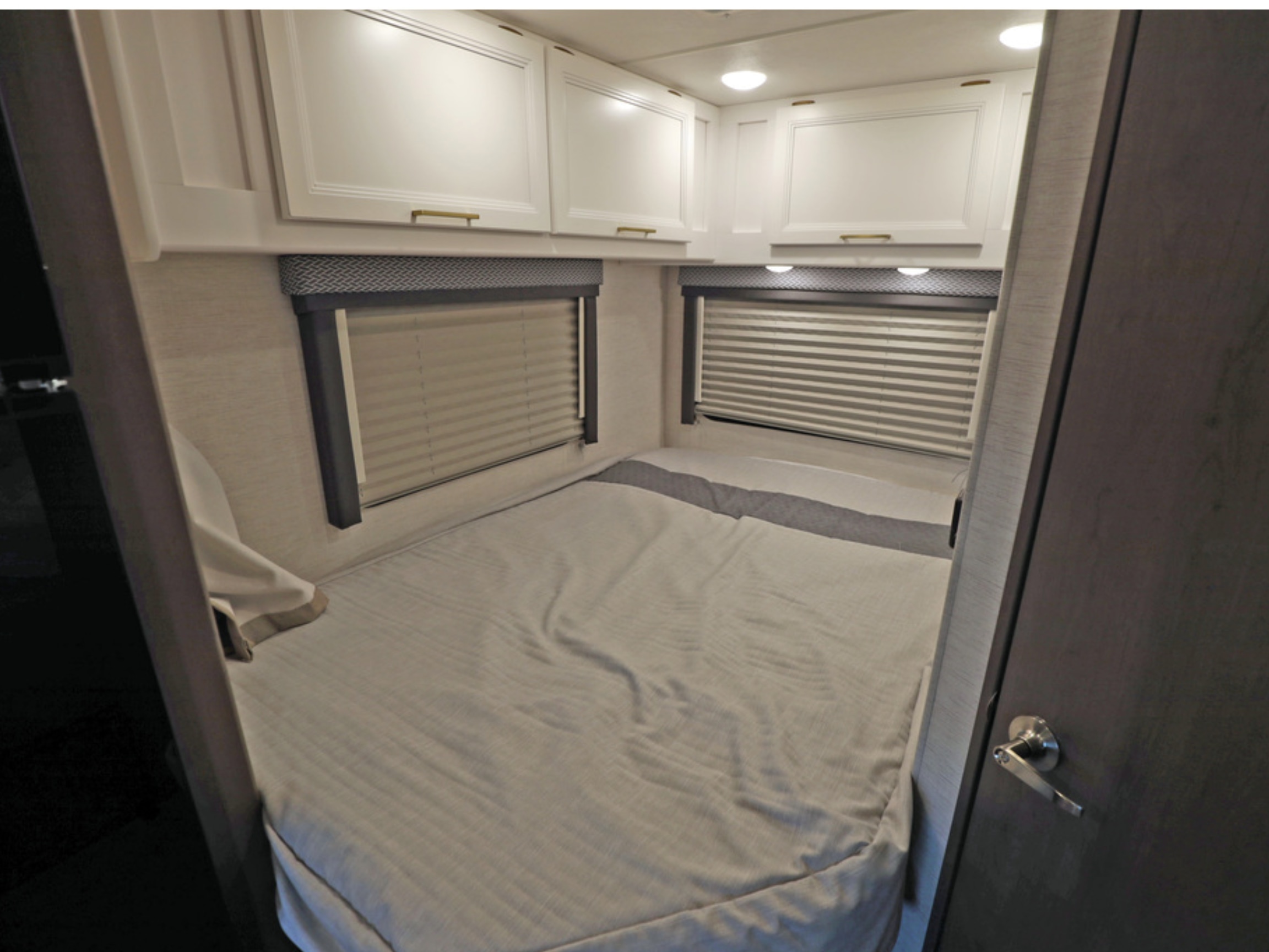 Experience comfort in this RV rental bedroom featuring a bed, overhead cabinets, and two windows with blinds.. Classe C 24'' sans extension Spare 2026