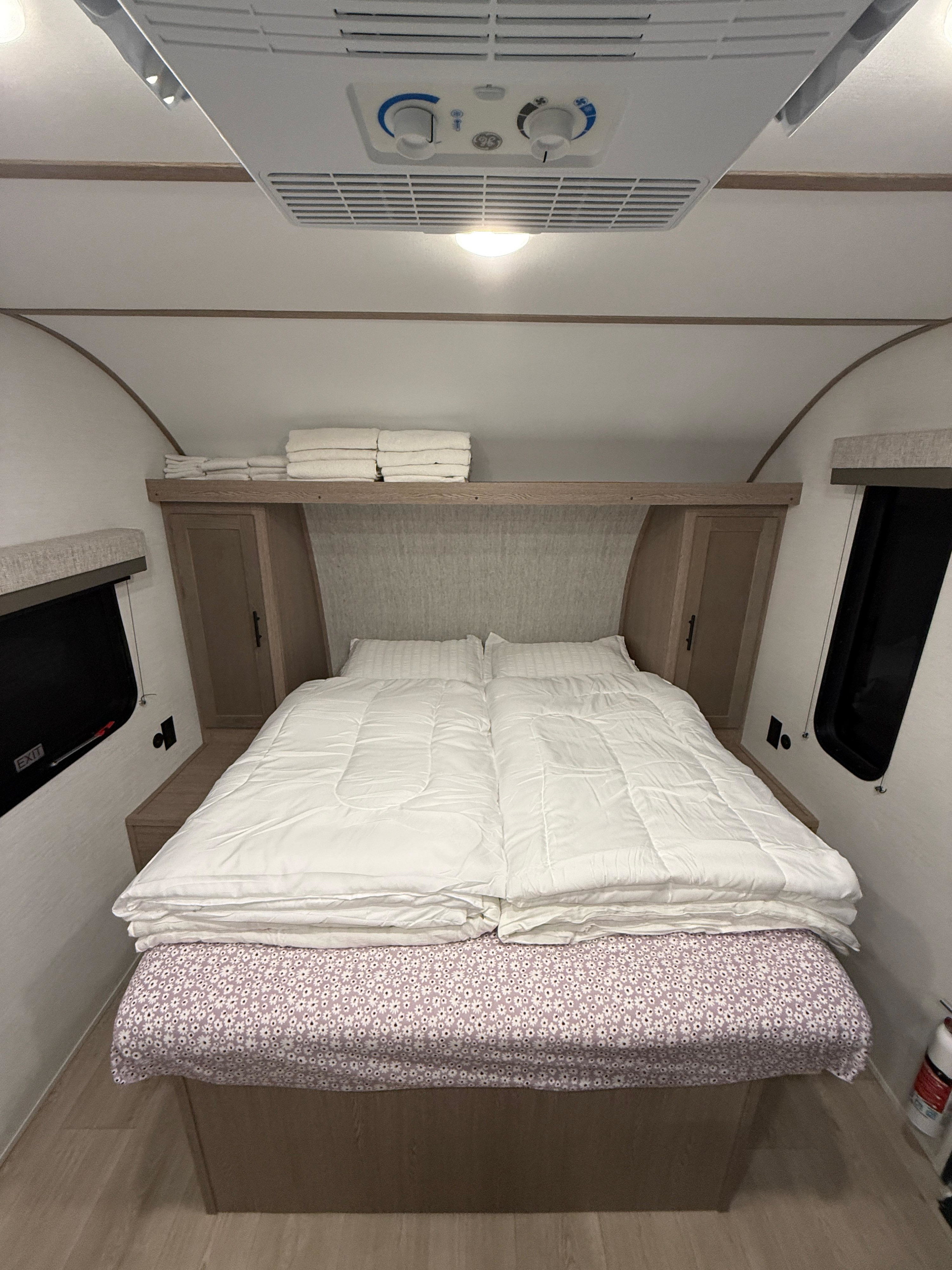 An RV rental bedroom featuring a neatly made bed with a floral sheet, overhead AC, storage, and windows, offering a cozy space.. Gulf Stream Ameri-Lite 2026