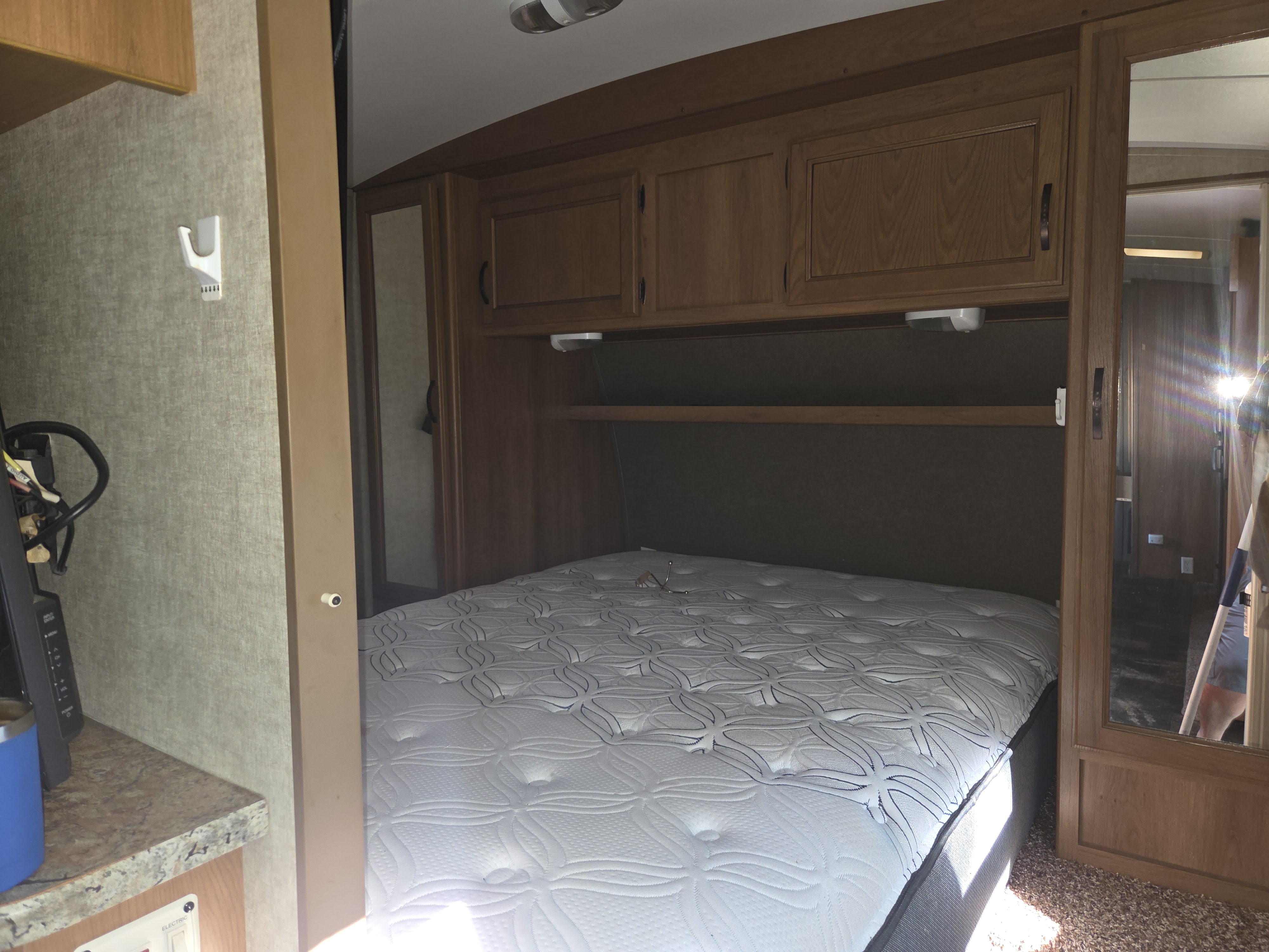 RV rental bedroom interior with a patterned mattress, overhead wooden cabinets, and mirrored closet door.. Keystone RV Outback Terrain 2013
