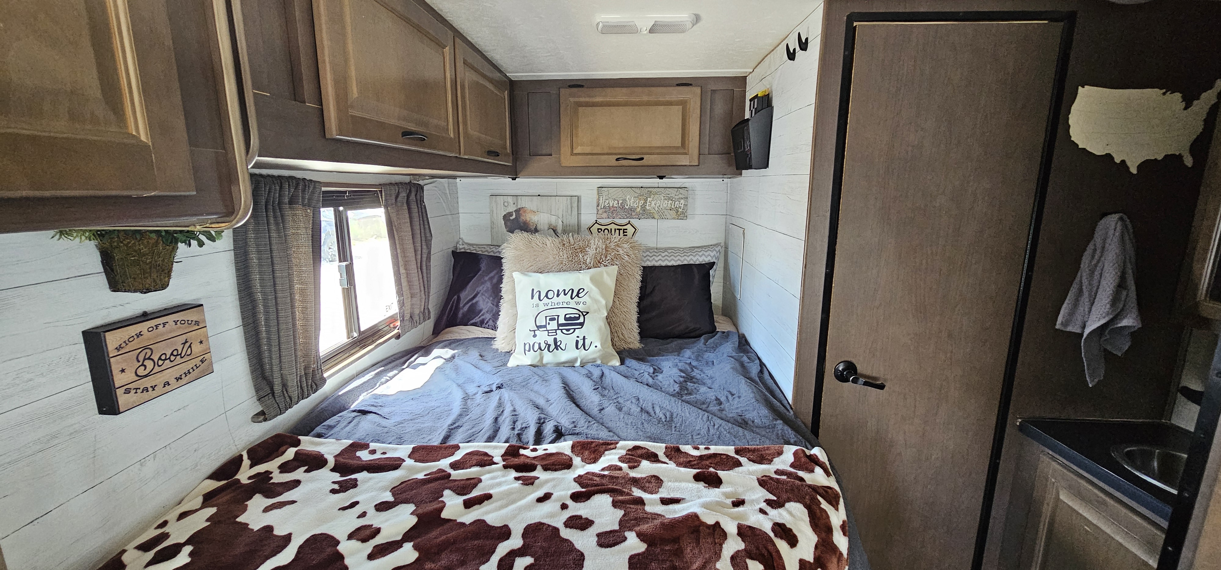 Cozy rv rental bedroom with themed decor, a cow-print blanket, and "home is where we park it" pillow, ideal for travel.. Thor Majestic 2019