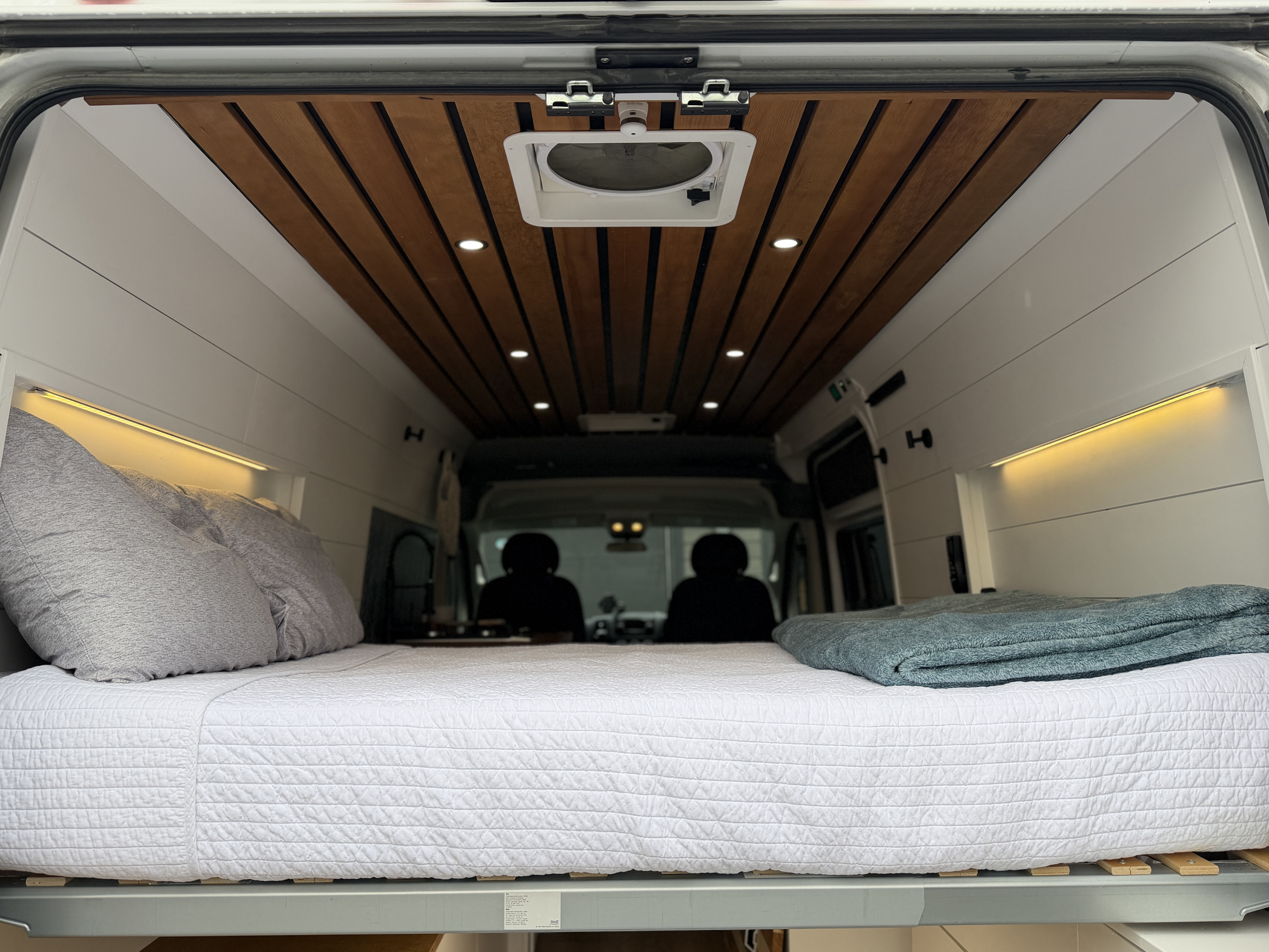 Cozy camper van interior for your next RV rental, featuring a comfortable bed, warm lighting, and a stylish wooden ceiling.. Custom Promaster 2500 2019