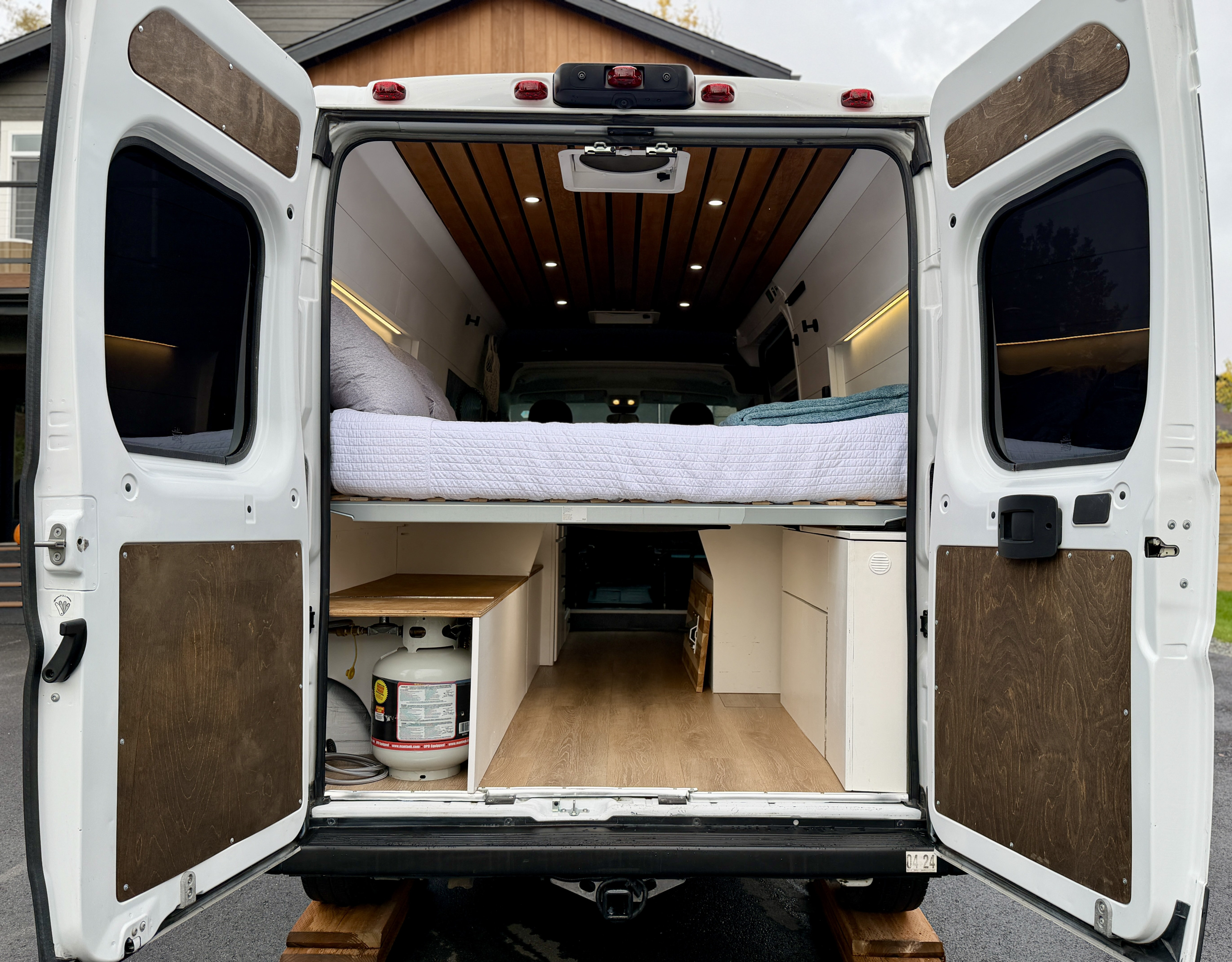 RV rental: Open rear of a white camper van conversion, showcasing its bed, wood-paneled interior, and under-bed storage.. Custom Promaster 2500 2019