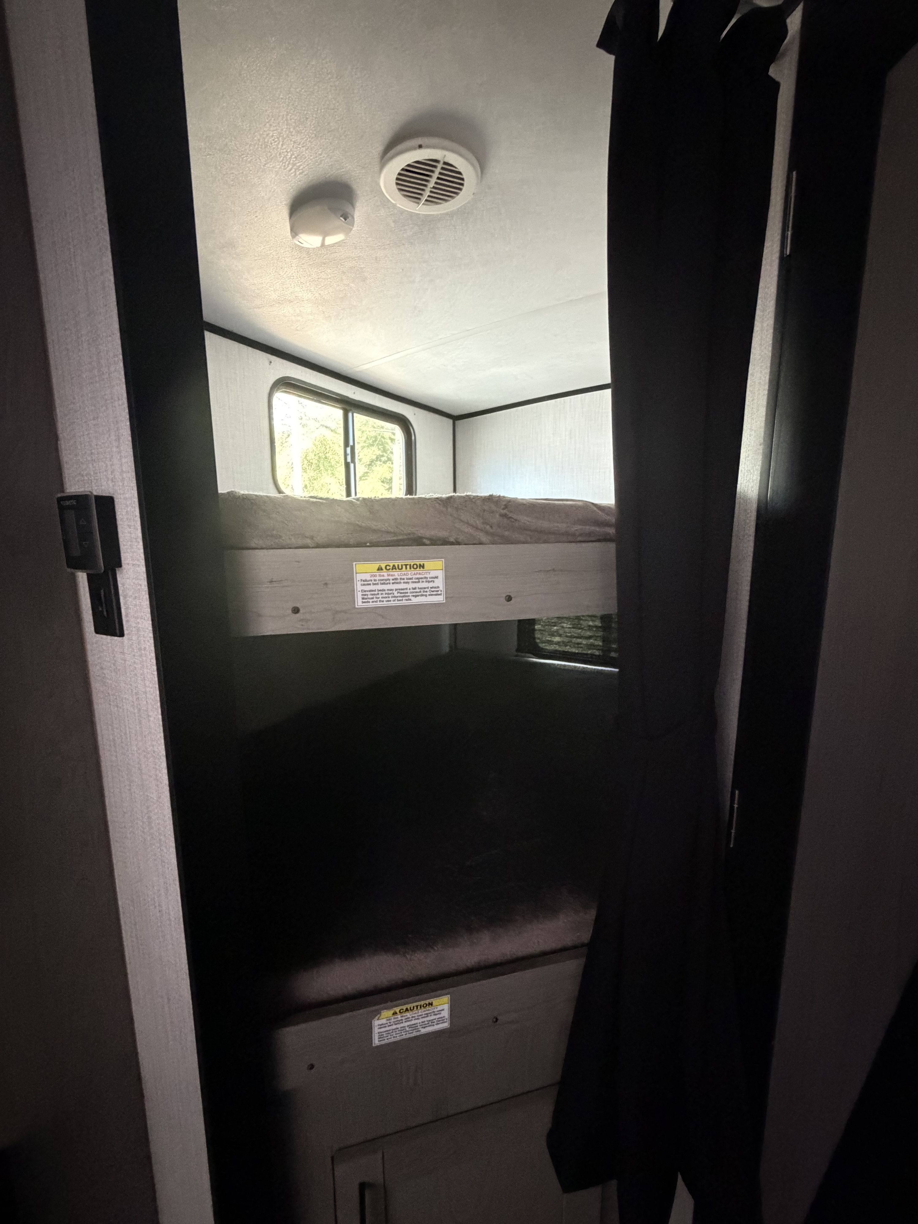 Cozy rv rental interior featuring stacked bunk beds with a window, ceiling light, and vent. Caution labels visible on bed frames.. Heartland RVs Mallard 2021