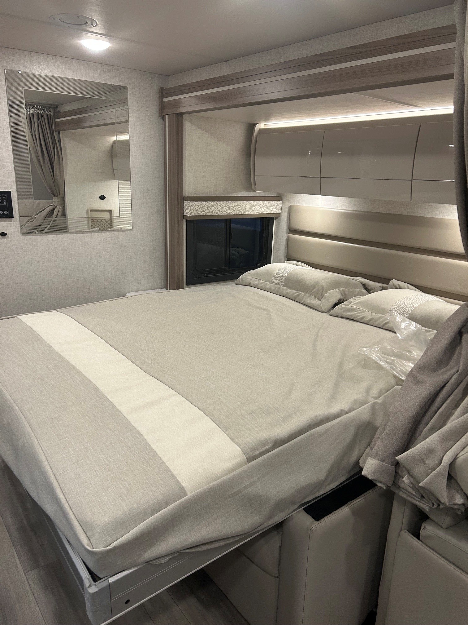 Inviting RV rental bedroom: light-toned bed with padded headboard, sleek overhead cabinets & storage. Bed base is lifted.. Thor Delano 2026
