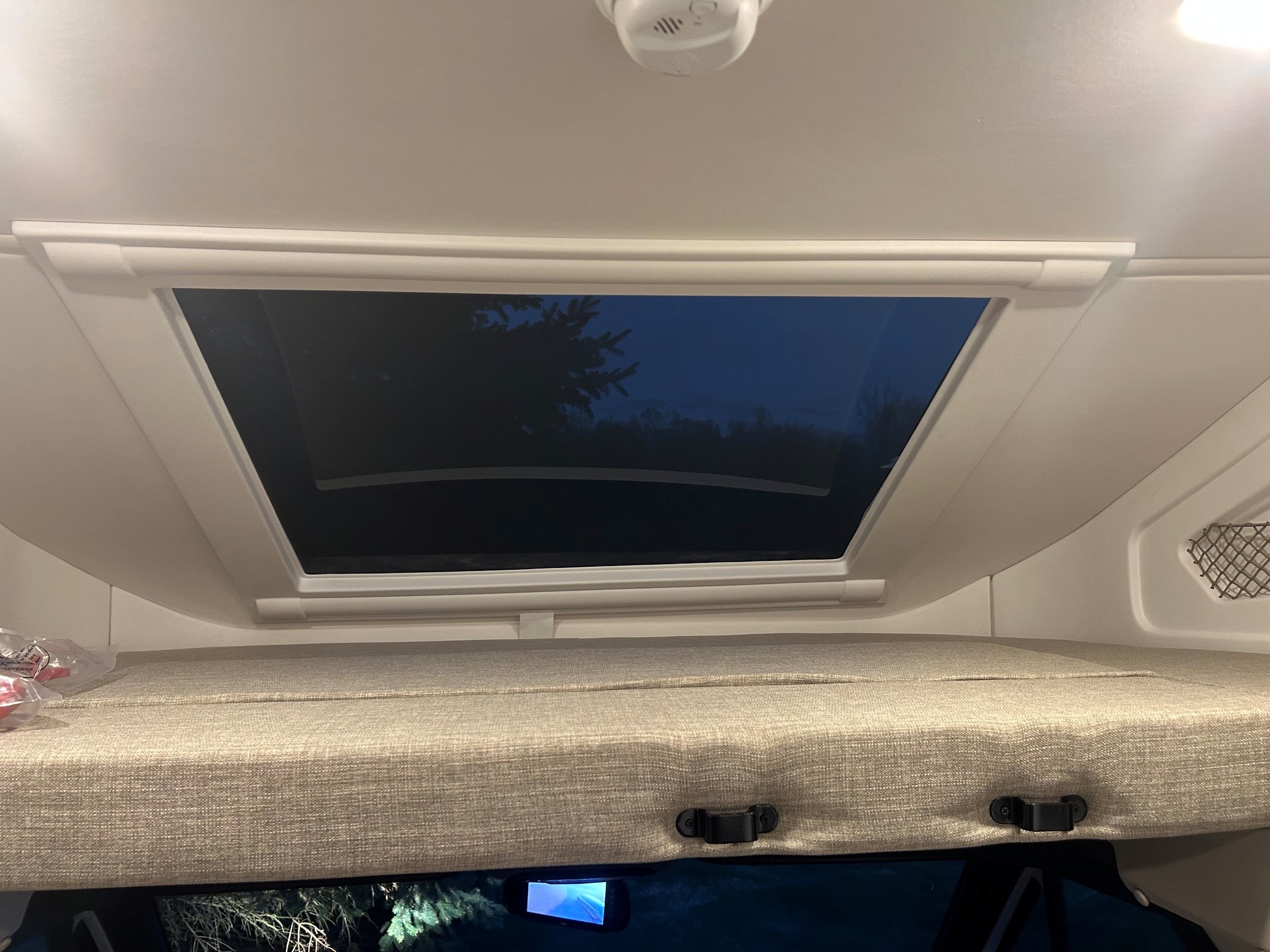 Cozy overhead bunk and skylight in an rv rental, offering a peaceful night view of trees and sky. Ideal for sleeping under the stars.. Thor Delano 2026