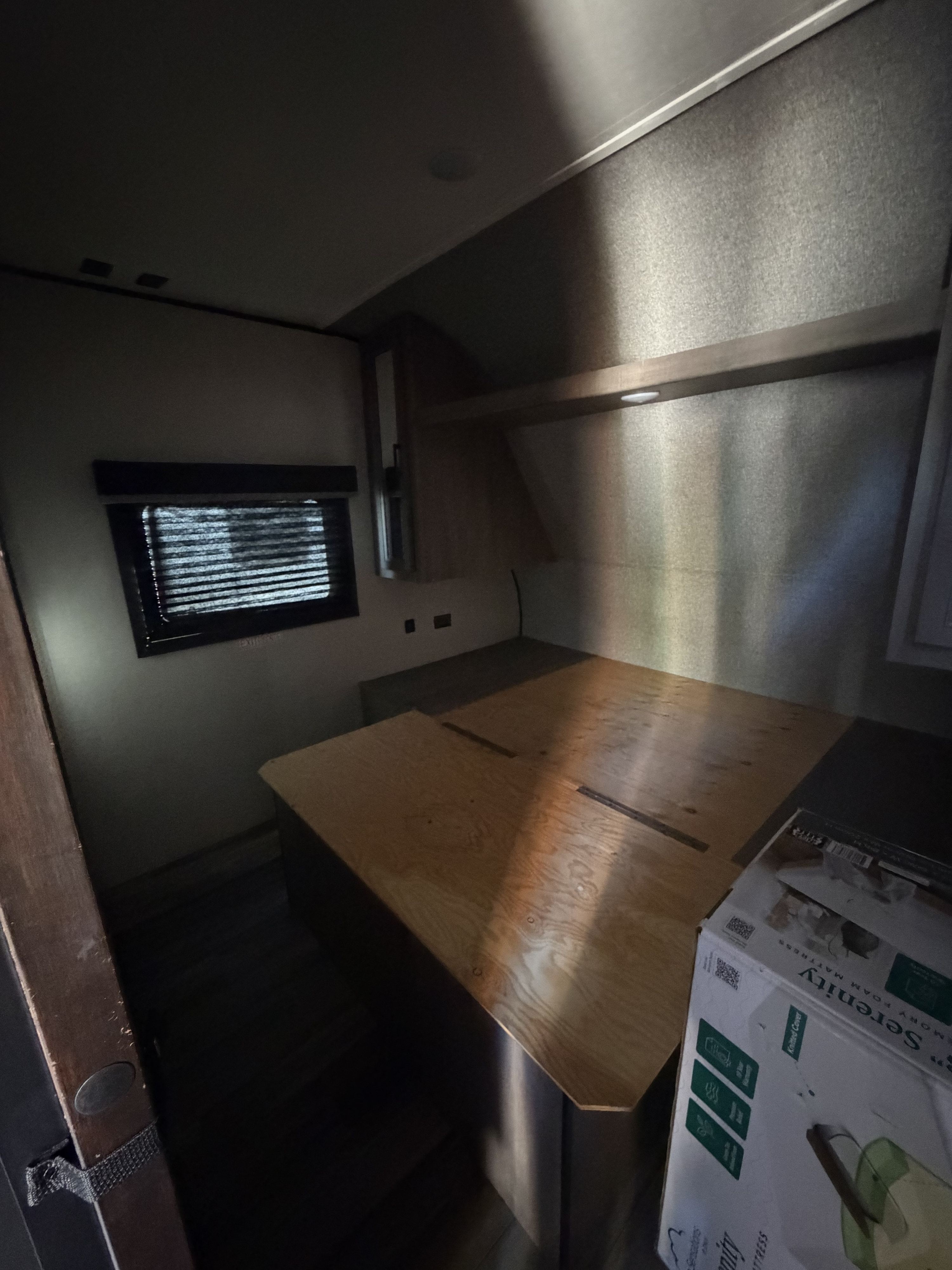 Interior of an RV rental bedroom featuring a wooden bed base, window with blinds, overhead light, and a new mattress in a box.. Starcraft Autumn Ridge 2022