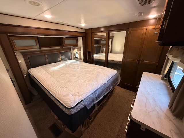 Spacious RV rental bedroom featuring a queen bed with new mattress, wooden cabinetry, mirrored closet, and dresser.. Crusader Crusader Fifth Wheel 2019