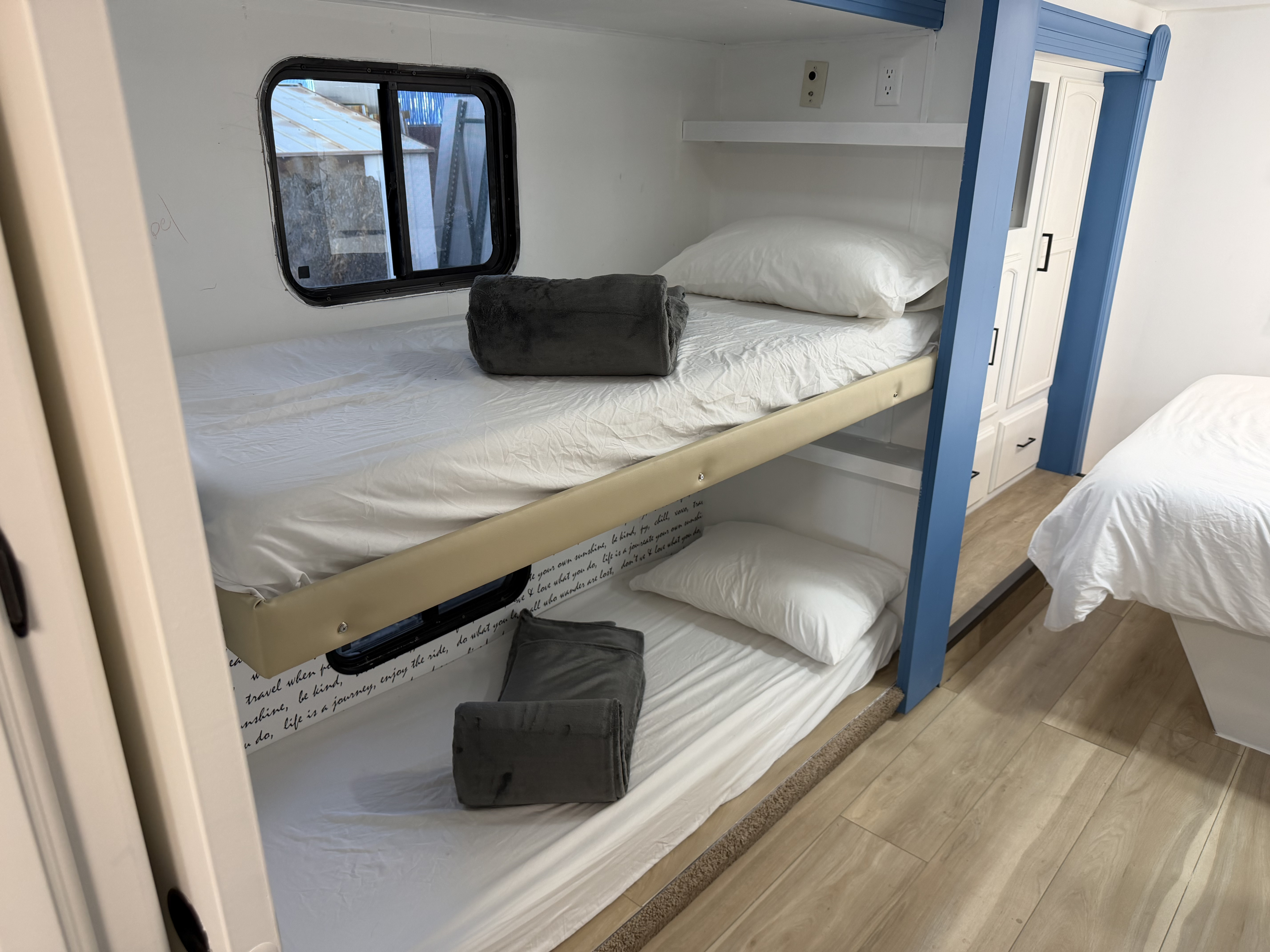Cozy RV rental interior featuring comfortable bunk beds with white bedding, gray blankets, and a window. Blue frame and wood floor.. Forest River Coachmen 2012