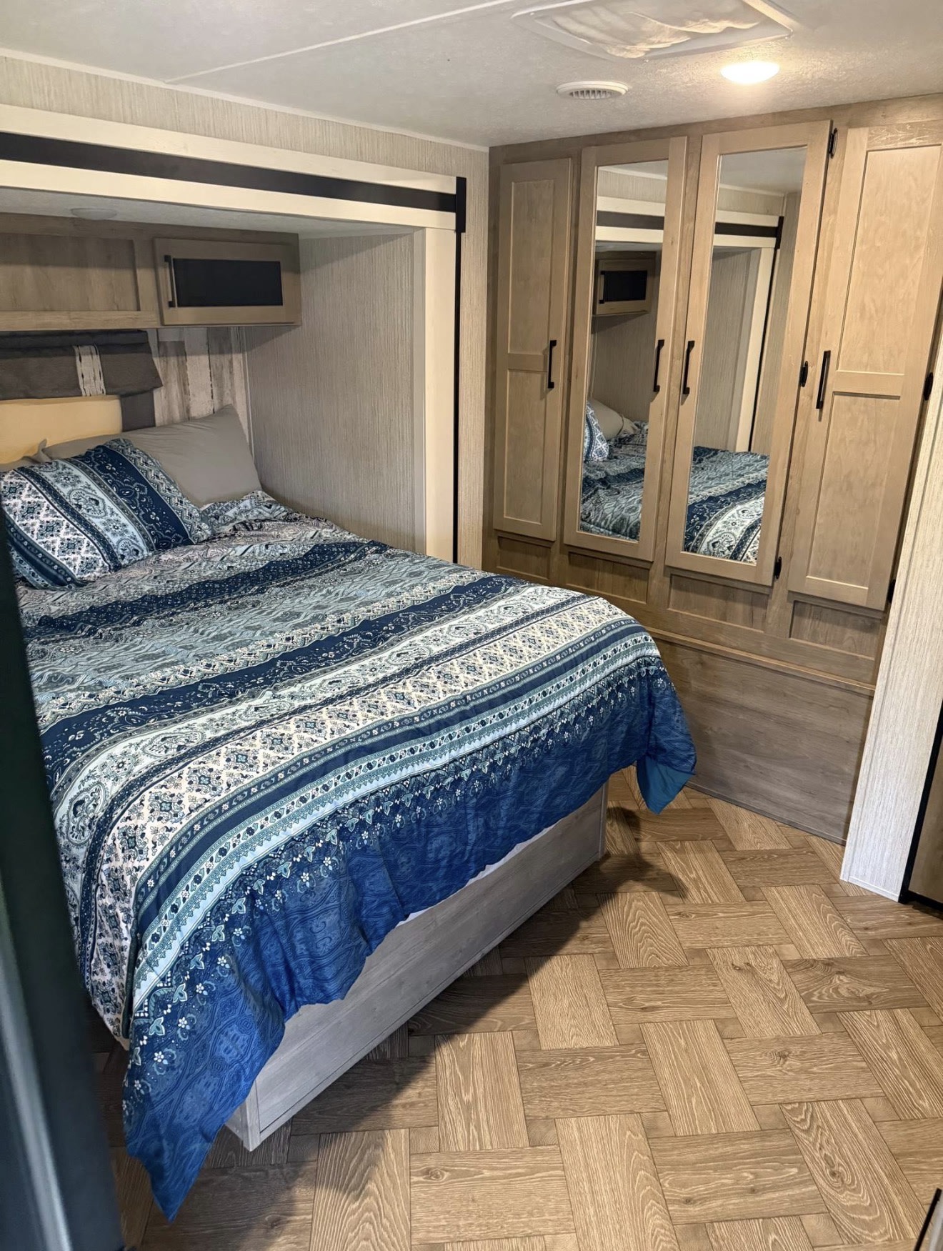 Inside a comfortable RV rental, featuring a bedroom with blue bedding, mirrored wardrobe, and wood floors. Perfect for road trips.. Forest River Palomino Puma 2022