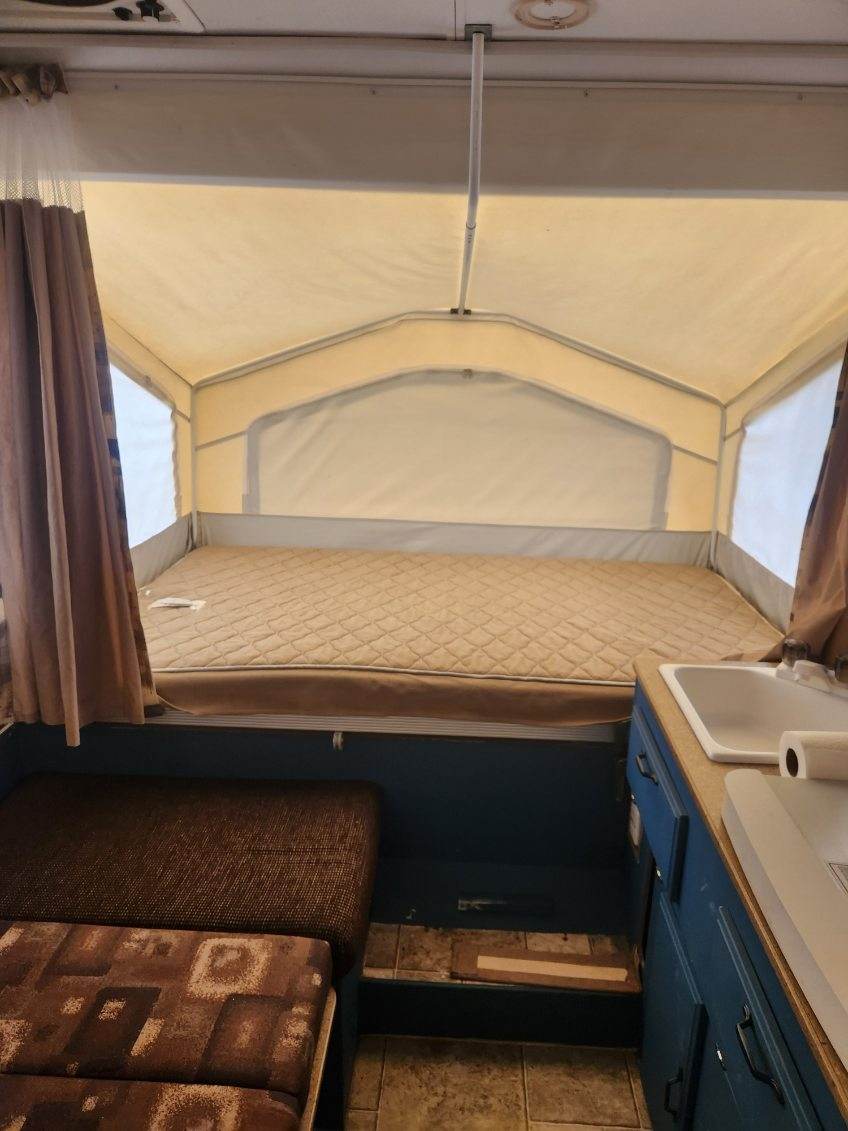 Cozy pop-up camper RV rental interior: bed, sink, and dining area. Ideal for camping adventures.. Forest River Rockwood Freedom 2009