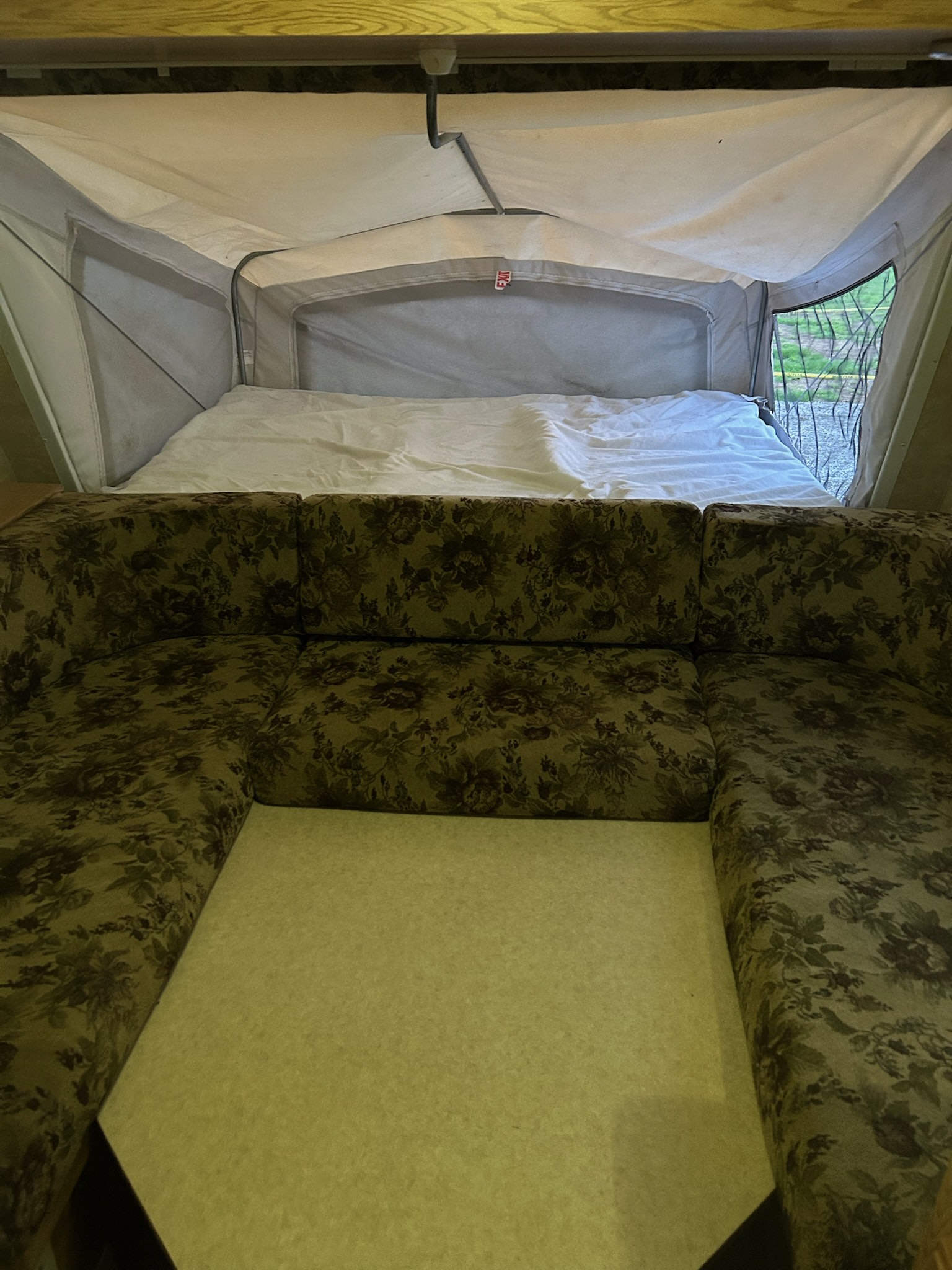 This RV rental's pop-up camper interior features a U-shaped floral sofa and a comfortable bed.. KZ CCH 2005