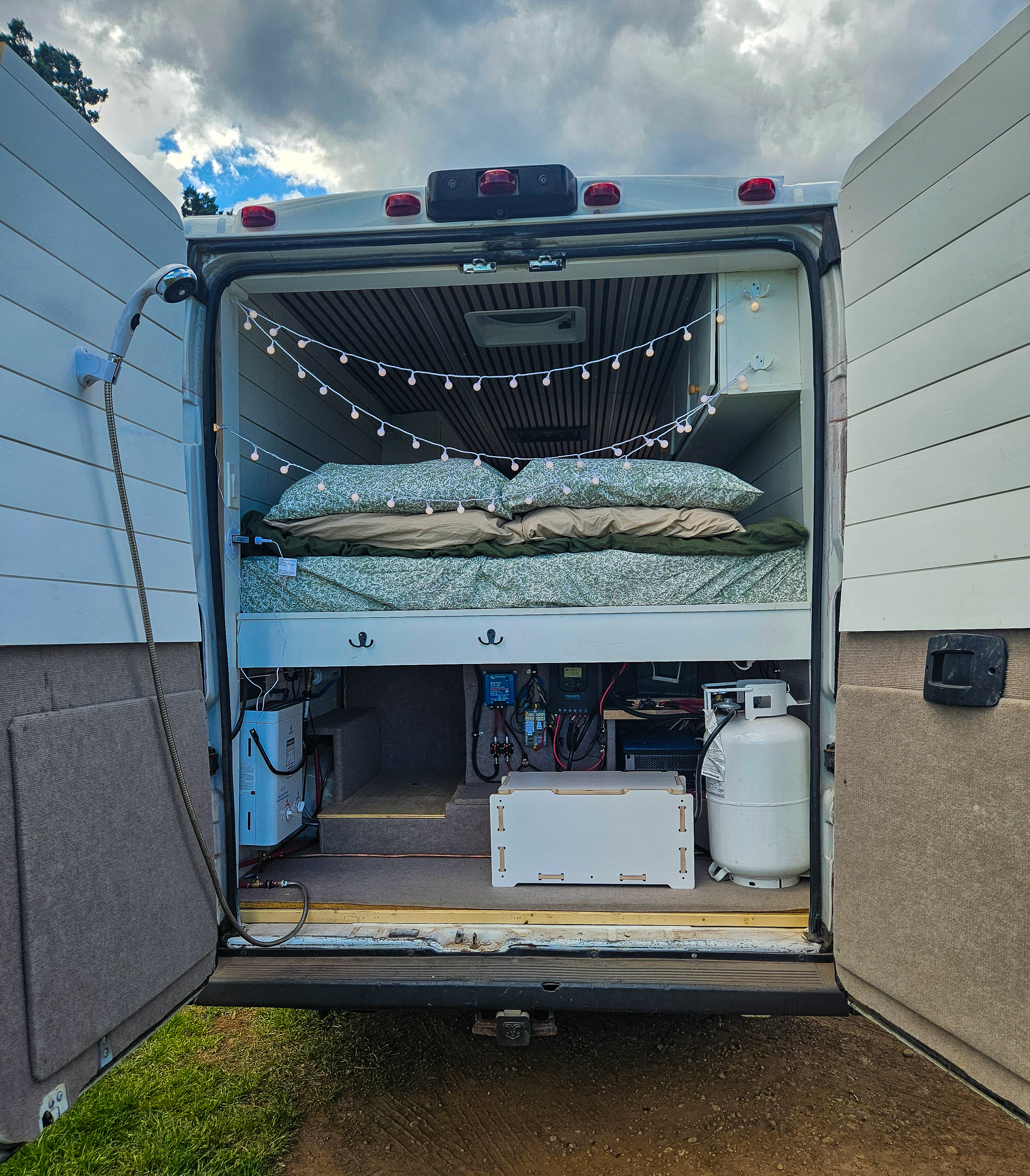 RV rental van interior showcasing a cozy bed, outdoor shower, essential power systems, and propane for your adventures.. Ram ProMaster 2016