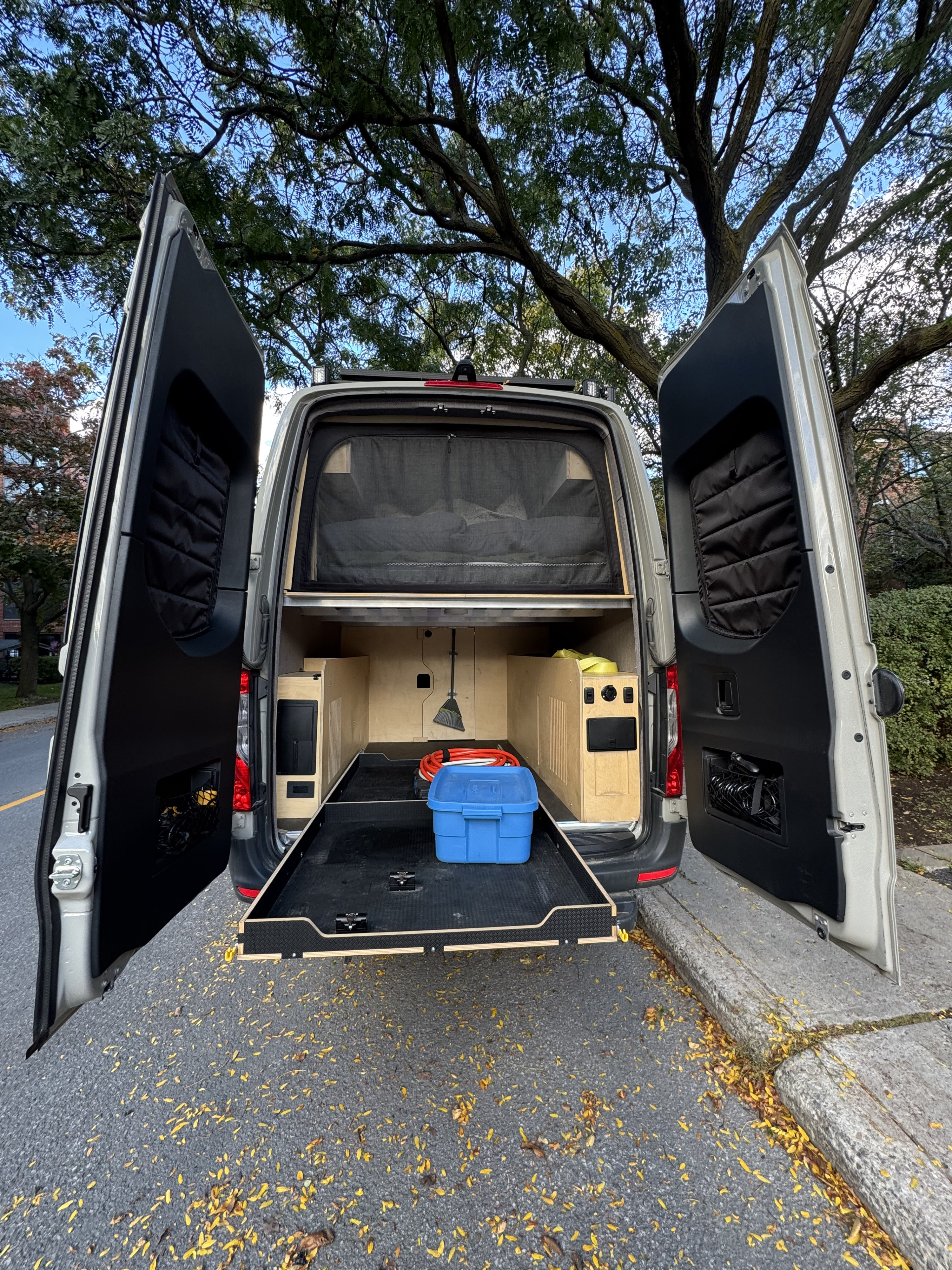 This RV rental's rear cargo area is open, revealing a pull-out tray, built-in storage, and a bed with a net.. Mercedes-Benz Sprinter 2026