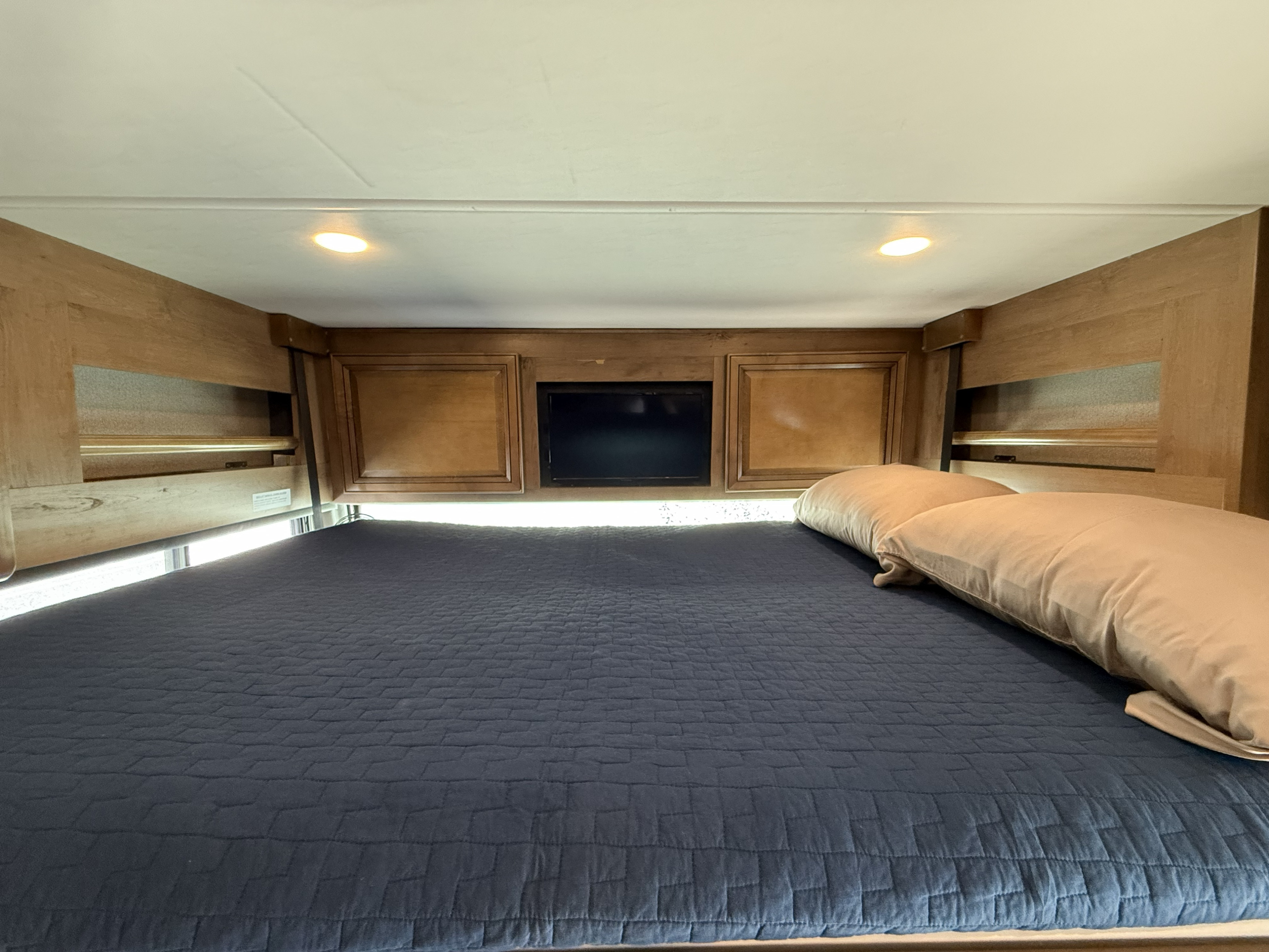 RV rental bedroom: a comfy blue quilted bed, wooden headboard with side shelving, and a mounted TV.. Fleetwood Southwind 37FP 2019