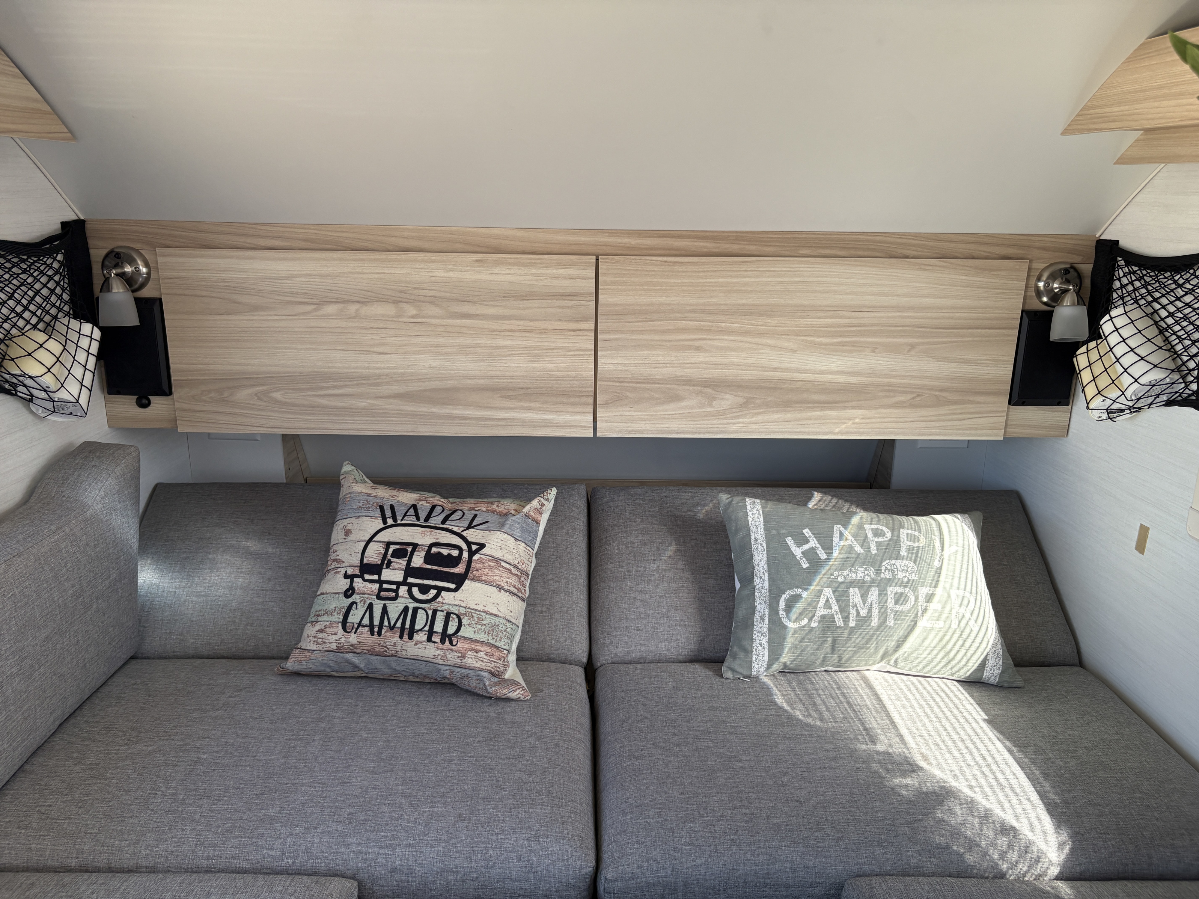 Cozy rv rental interior with grey seating, "Happy Camper" pillows, overhead storage, and reading lights.. nuCamp T@B 2024