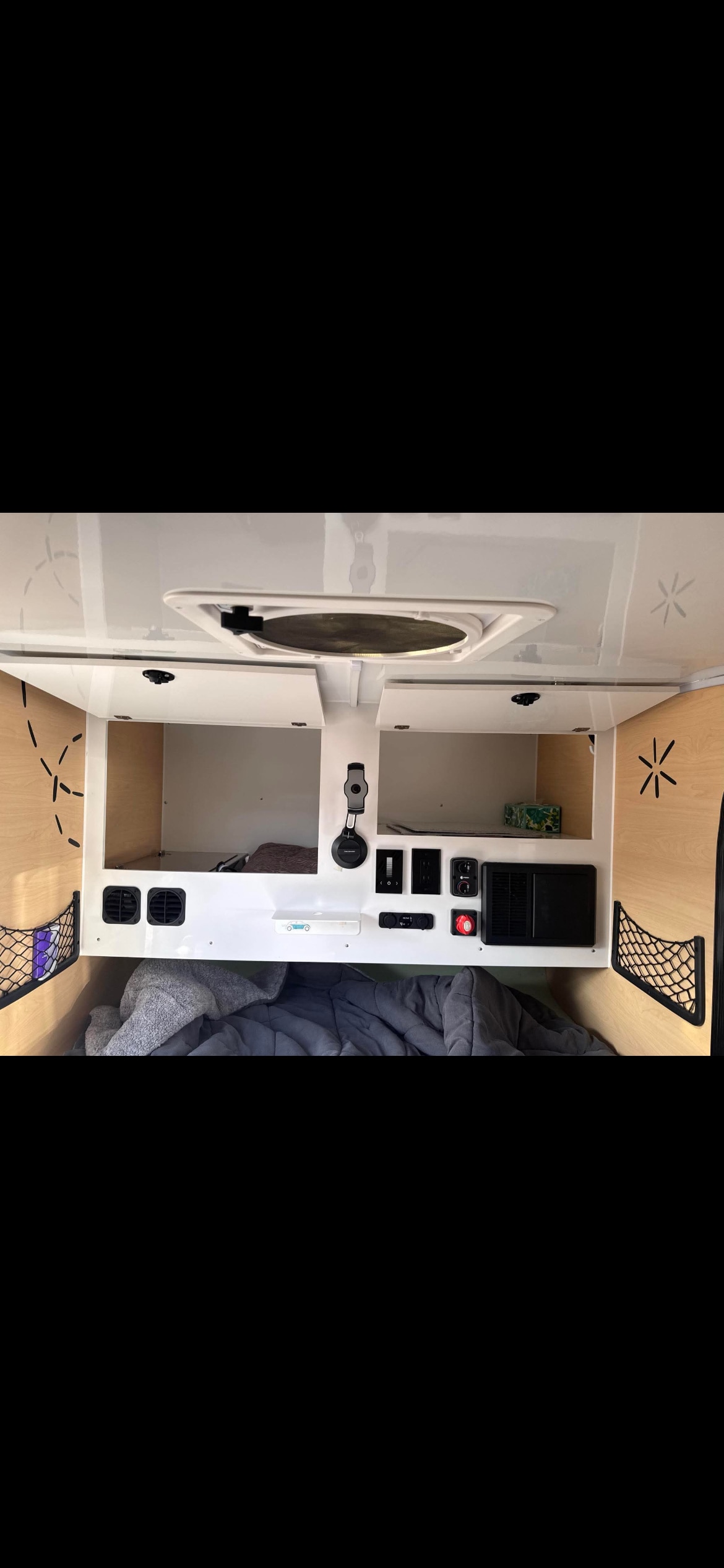 Inside a cozy RV rental: gray bedding, overhead storage, and a control panel with outlets. A compact camper interior for your trip.. Boreas MXT 2020