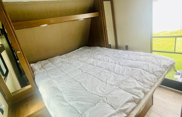 Cozy RV rental bedroom featuring a queen bed with a white comforter, overhead storage, and a bright window.. Aspen Trail Aspen Trail Trailer 2018
