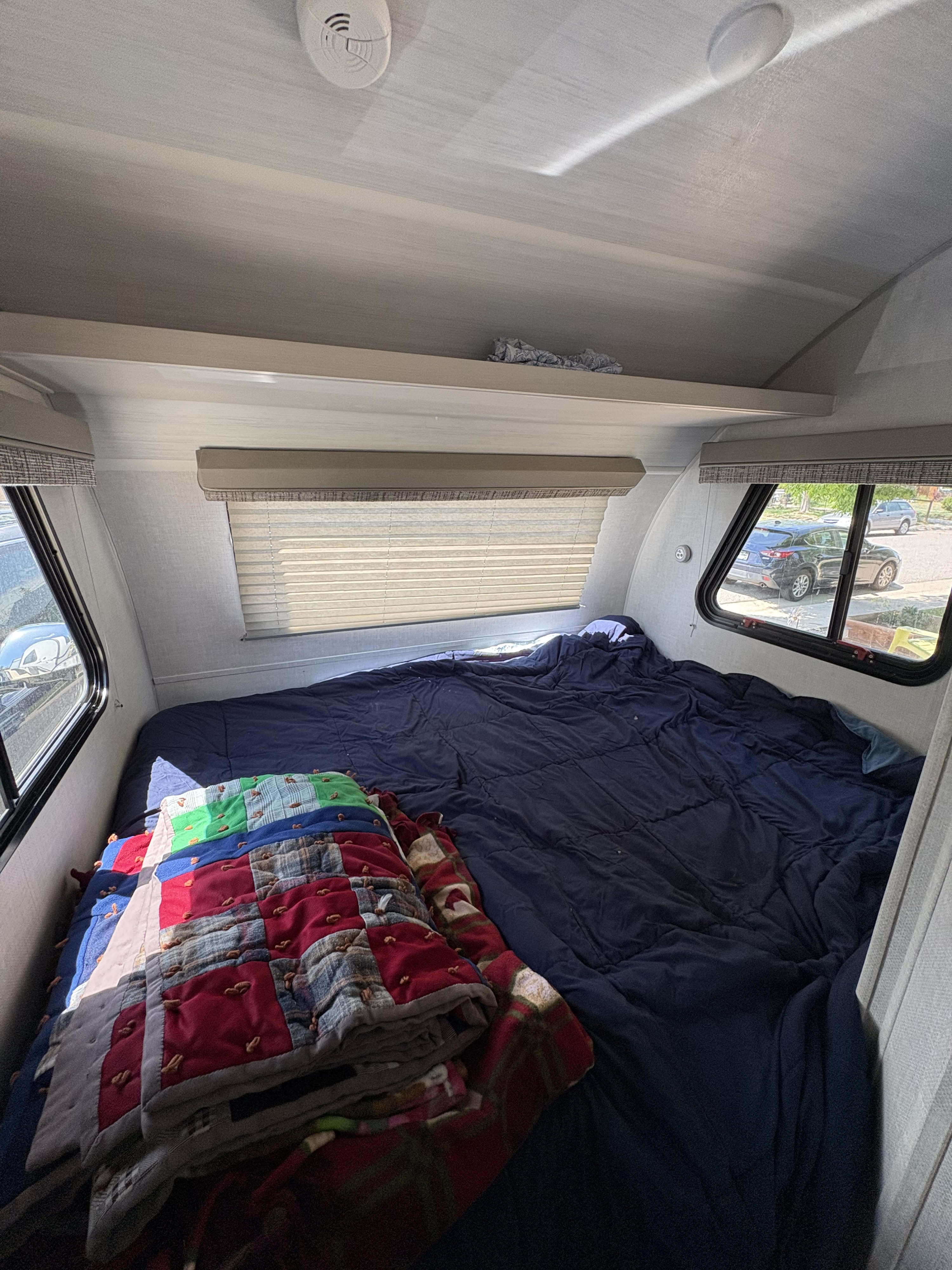 Cozy RV rental bedroom with a large bed, blue comforter, colorful quilt, and windows. Ceiling has a smoke detector.. R-Pod R-Pod Trailer 2021