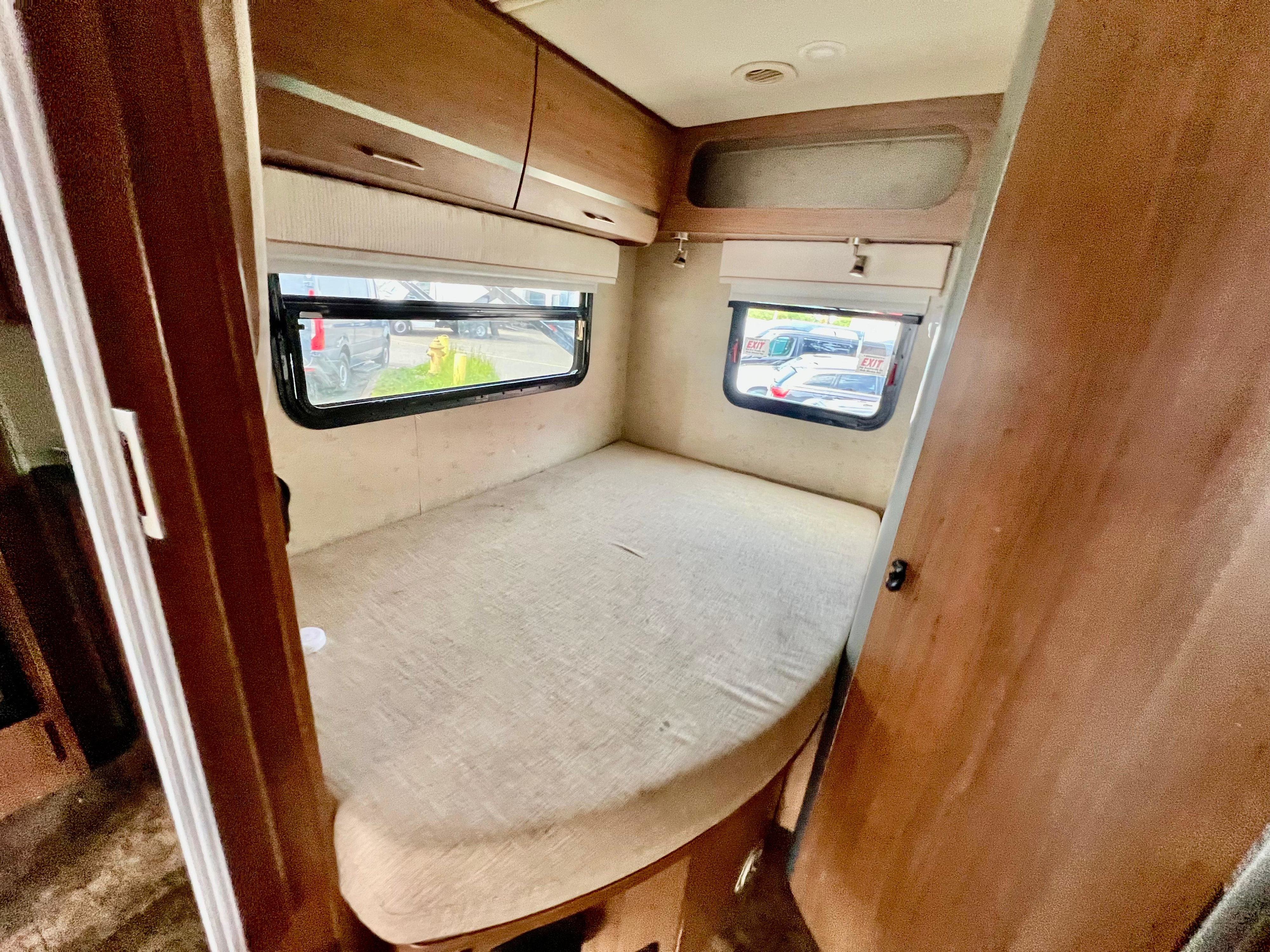 This RV rental's cozy bedroom features a built-in bed, windows with a view, and ample overhead storage cabinets.. Itasca Navion 2014