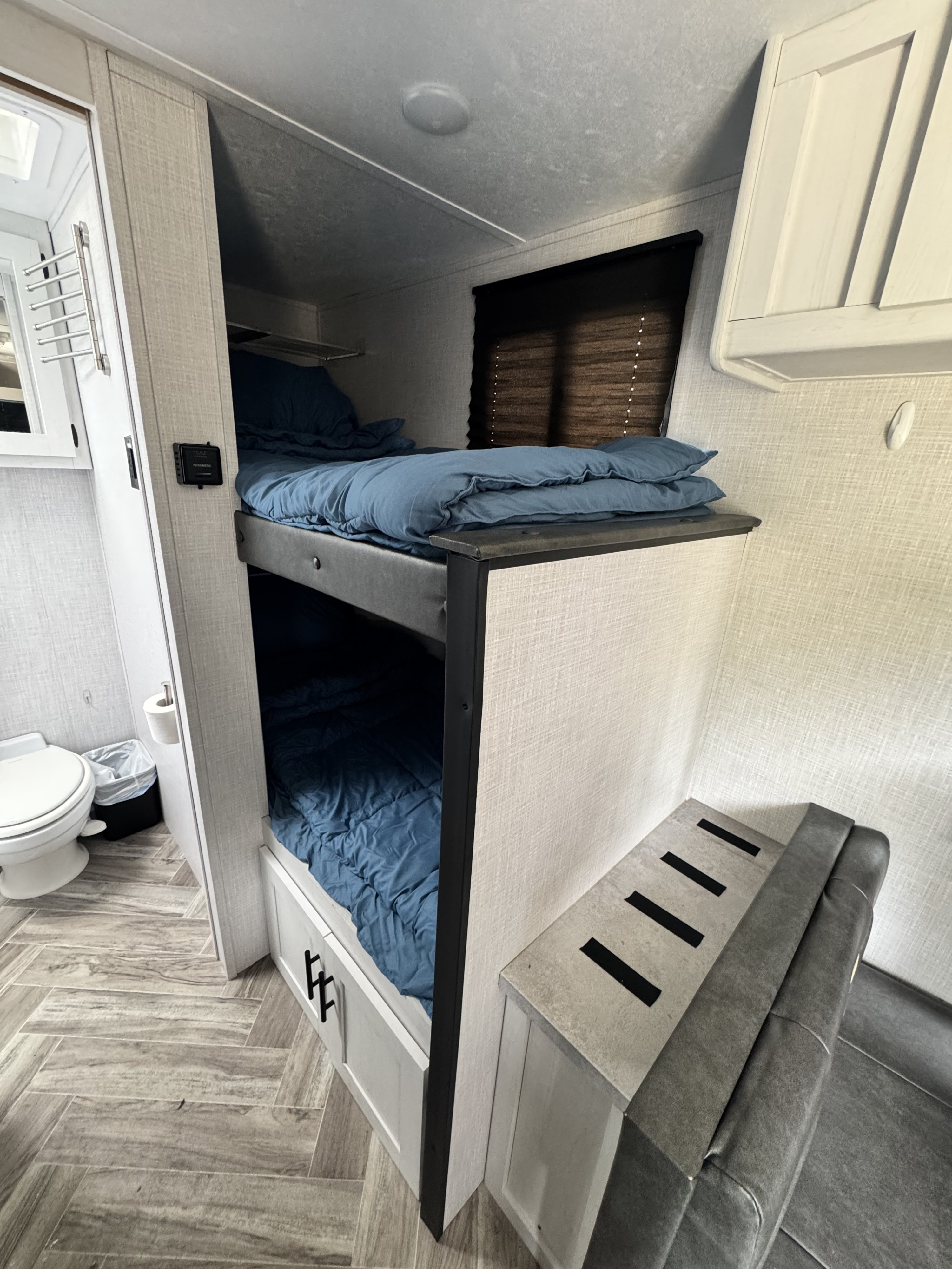 This RV rental features cozy bunk beds, an adjacent toilet, and a grey upholstered bench for comfortable living.. Dutchmen Coleman Rubicon 2023