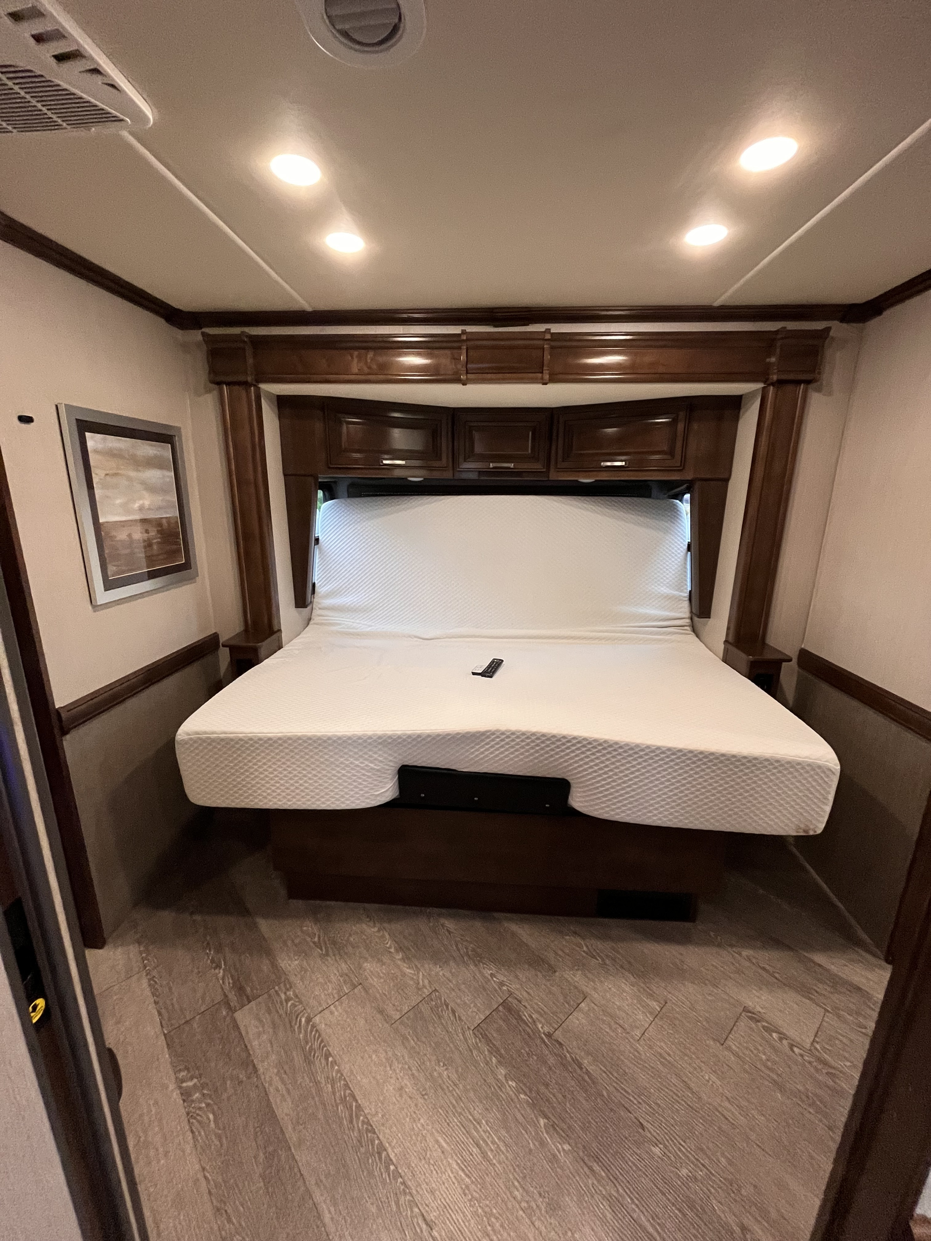 RV rental bedroom with an adjustable mattress, overhead storage, and dark wood cabinetry.. Fleetwood Pace Arrow 2020