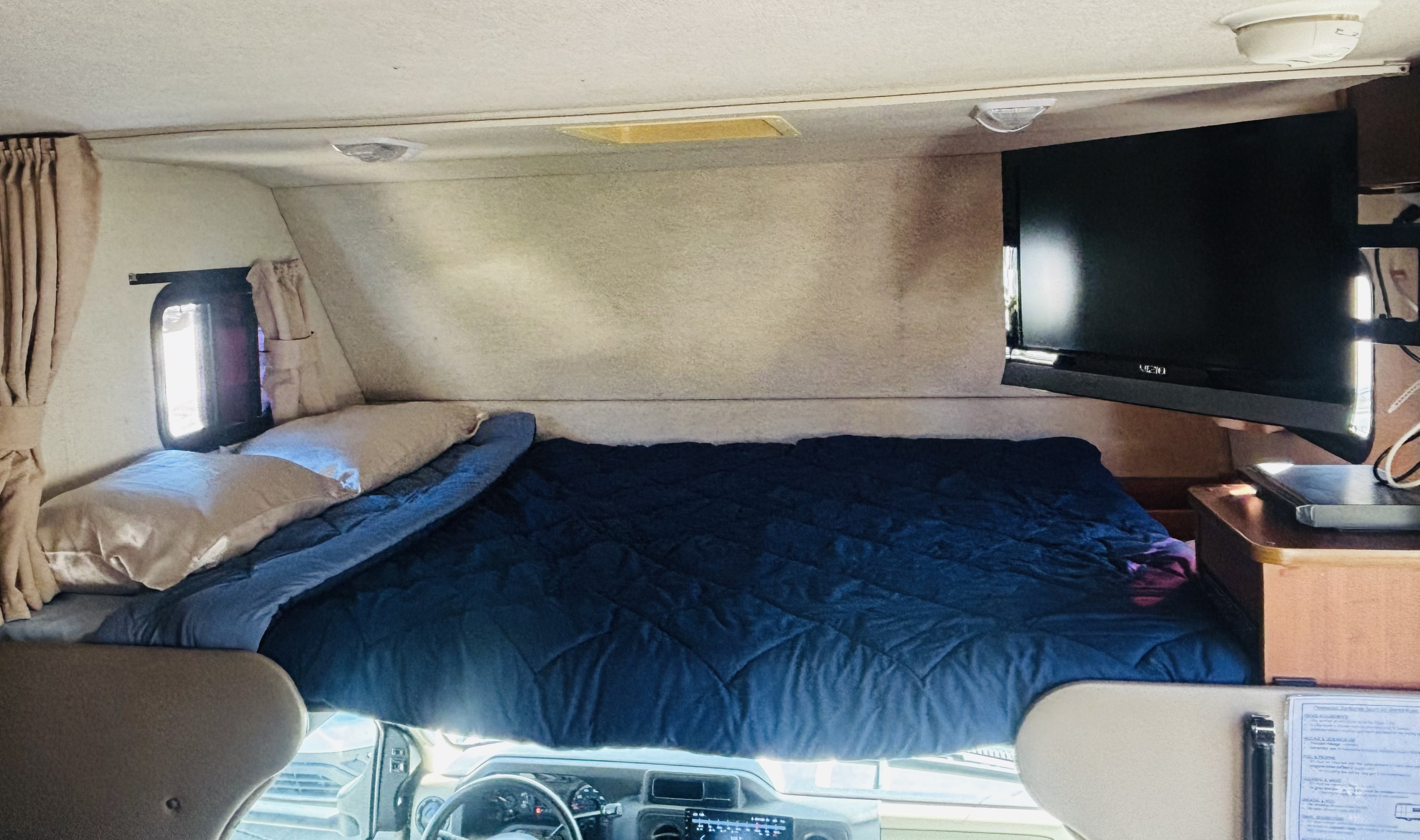 Inside an RV rental: a comfortable bed, TV, and window in the cab-over sleeping area, seen from the front.. Jamboree Sport 2011