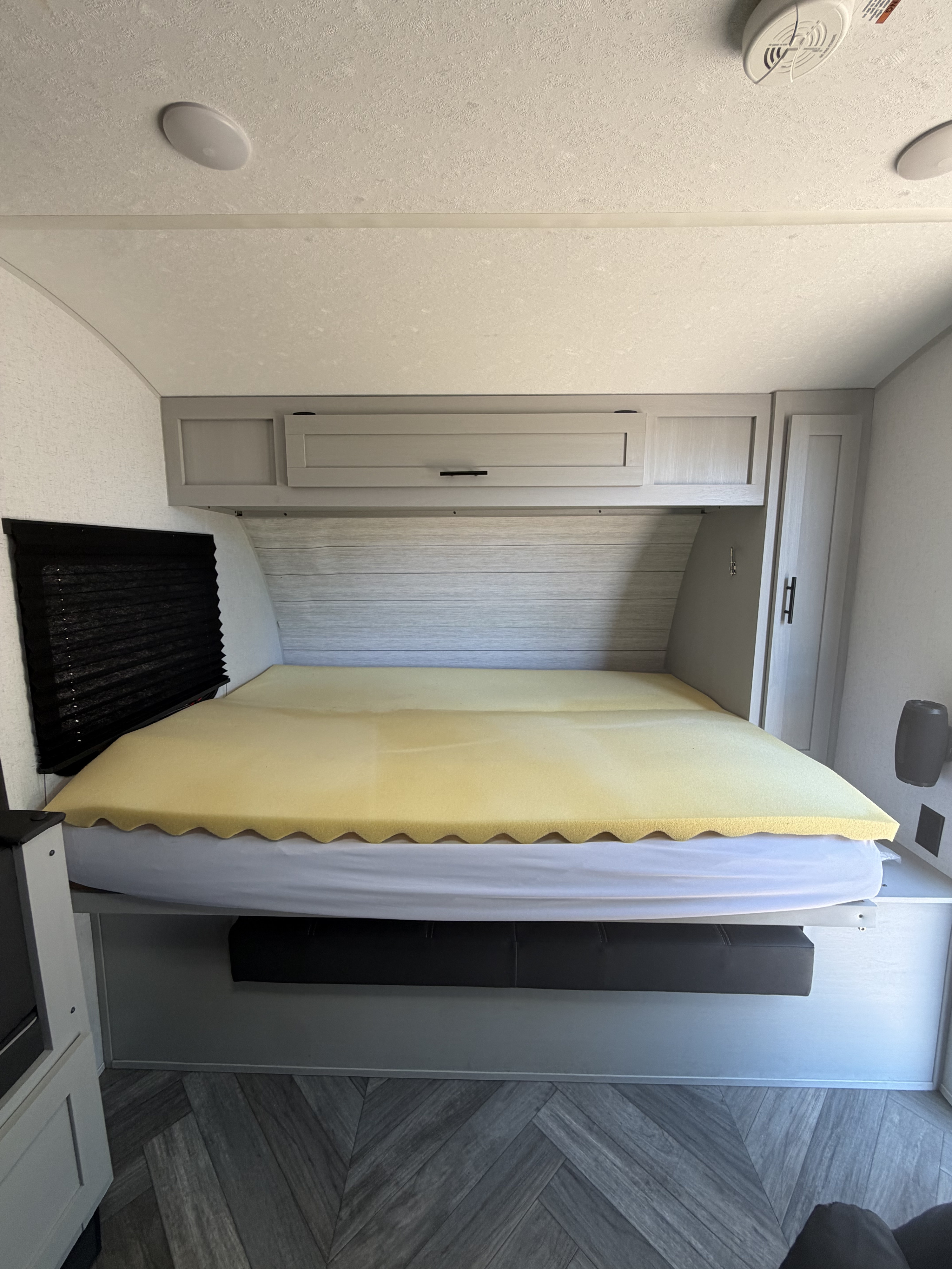 RV rental bedroom features a comfy bed with foam topper, overhead storage, and stylish herringbone flooring.. Forest River Wildwood FSX Plantium 2022