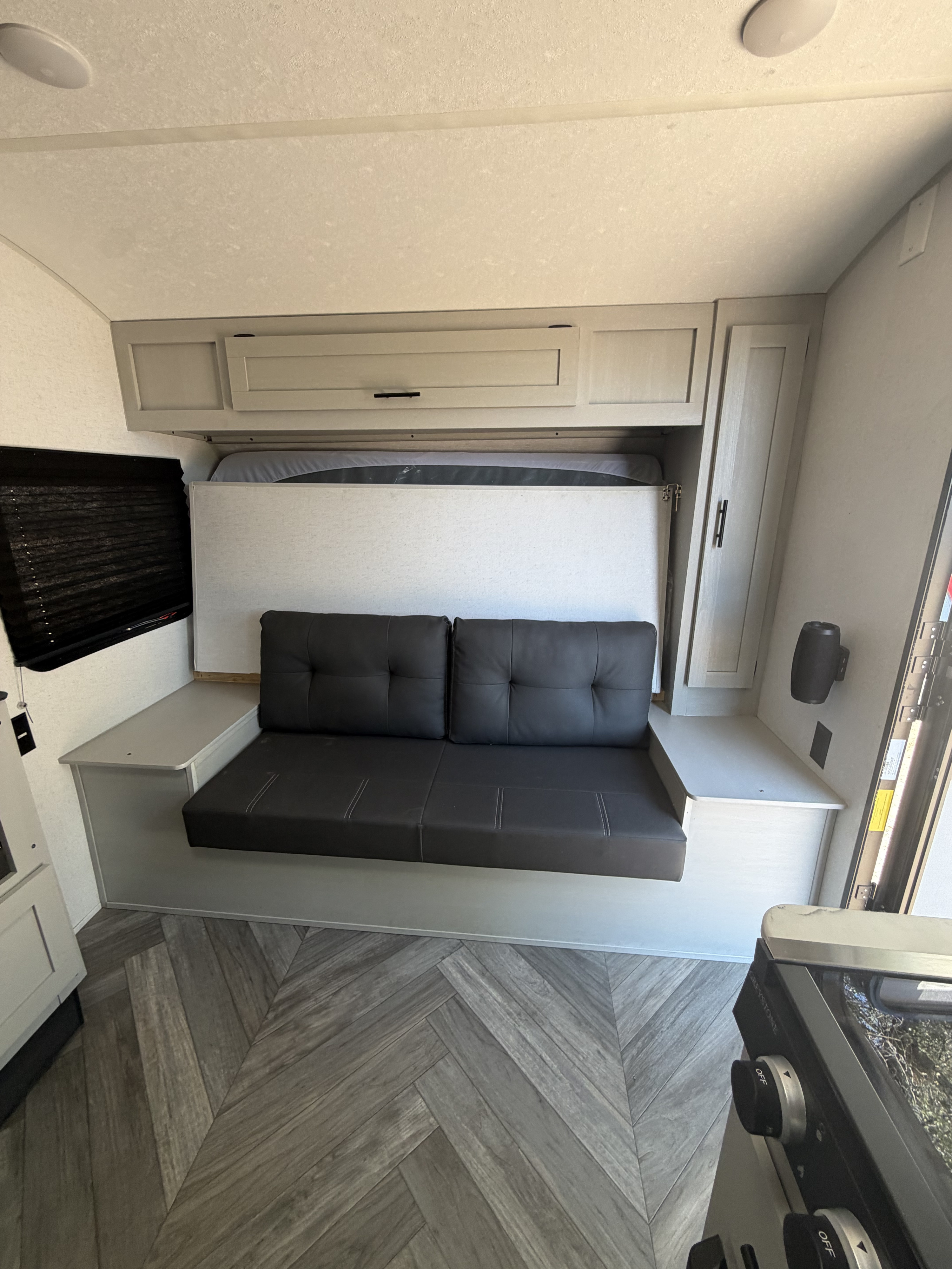 Cozy RV rental interior with a dark gray convertible sofa/bed, light wood cabinets, and herringbone-patterned flooring.. Forest River Wildwood FSX Plantium 2022