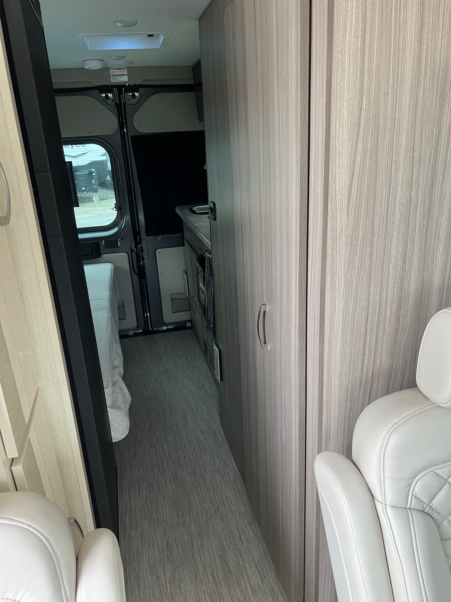 Inside a modern **rv rental**, looking towards the rear. Features a light-toned interior with a bed, galley, & captains chair.. Jayco Swift Li 2023