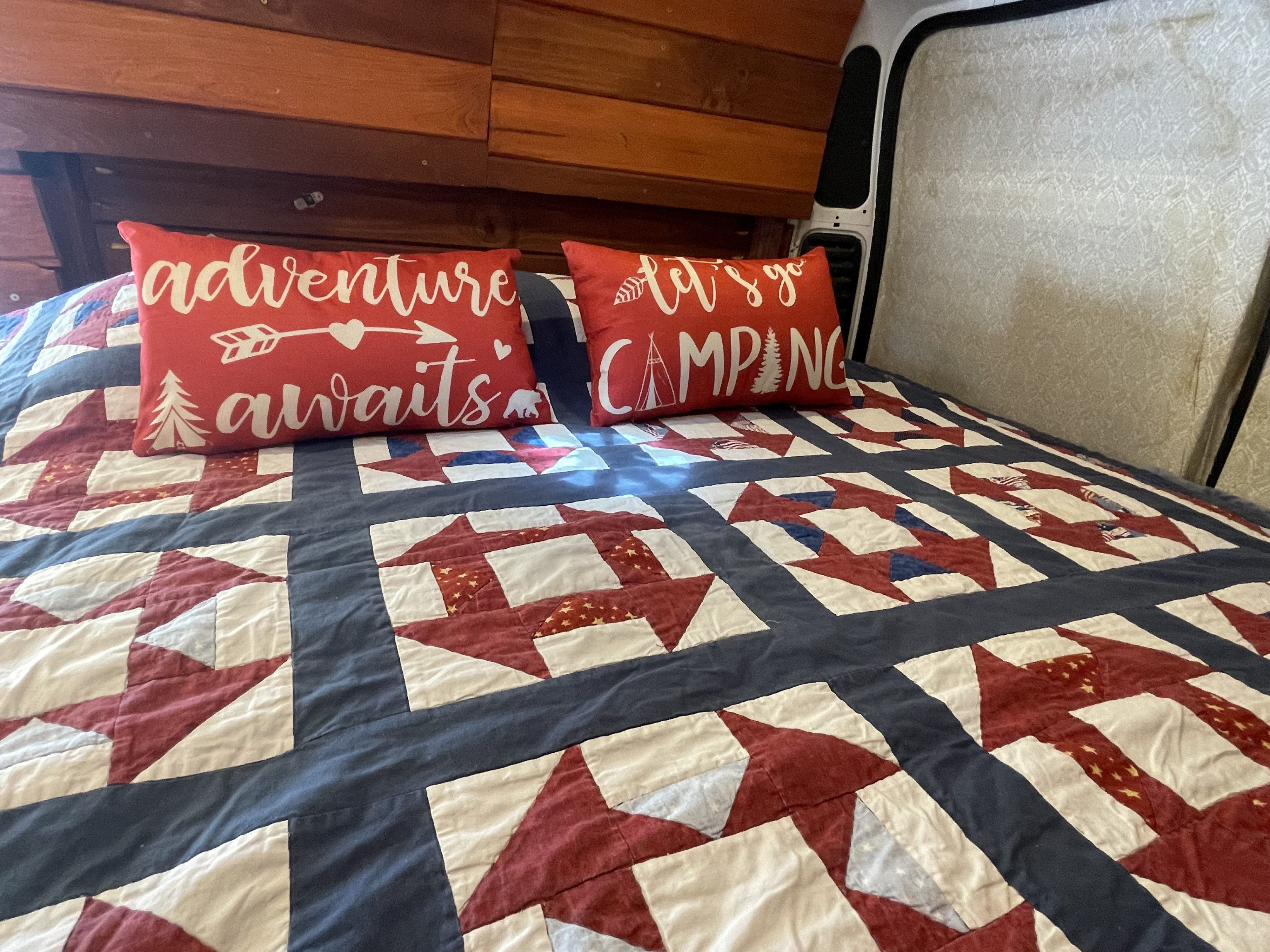 Cozy RV rental bedroom featuring a patriotic quilt and "adventure awaits" and "let's go camping" pillows.. Dodge Other 2021