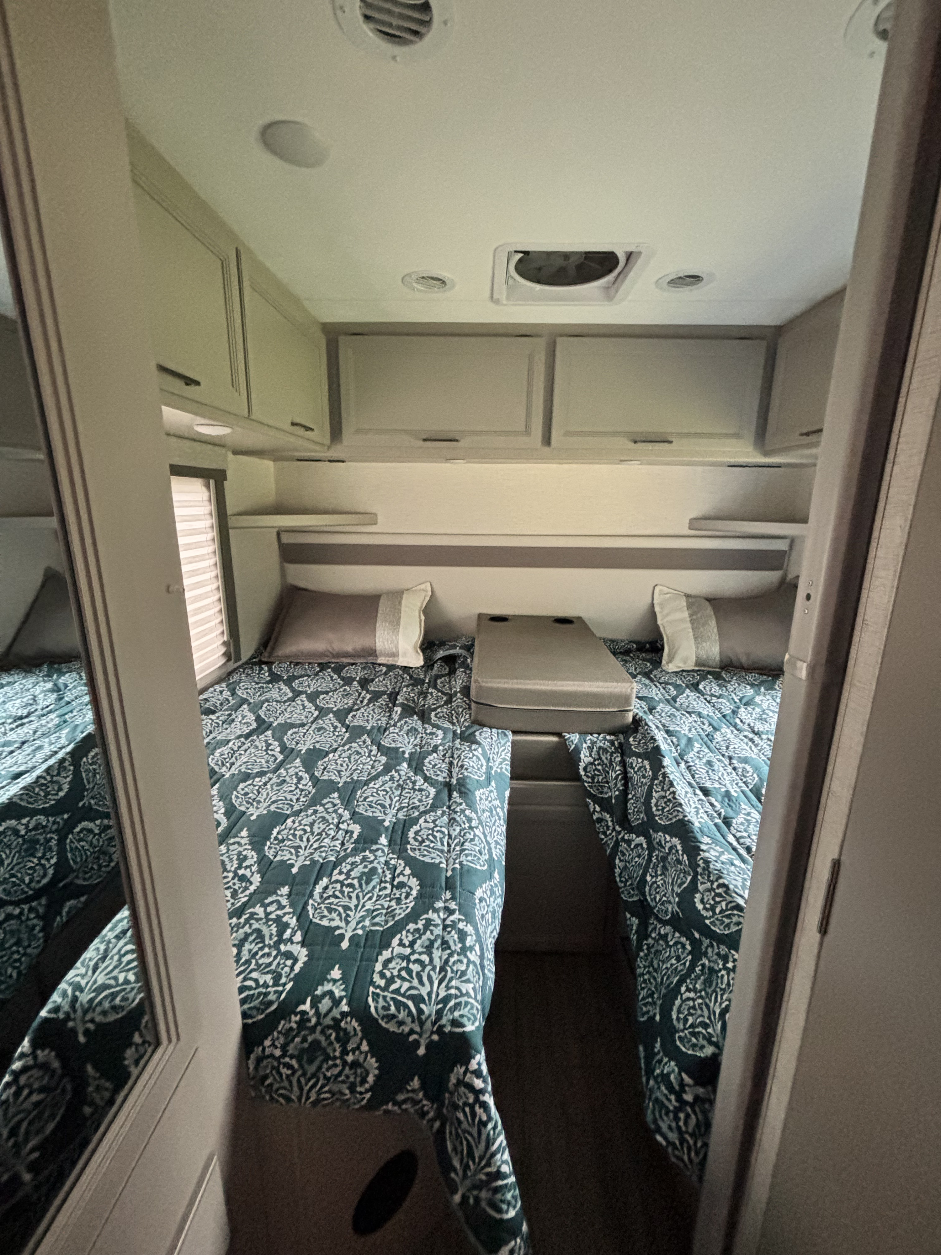 Cozy RV rental bedroom featuring two twin beds with teal patterned bedding, overhead storage, and a shared console.. Thor Four Winds 2025