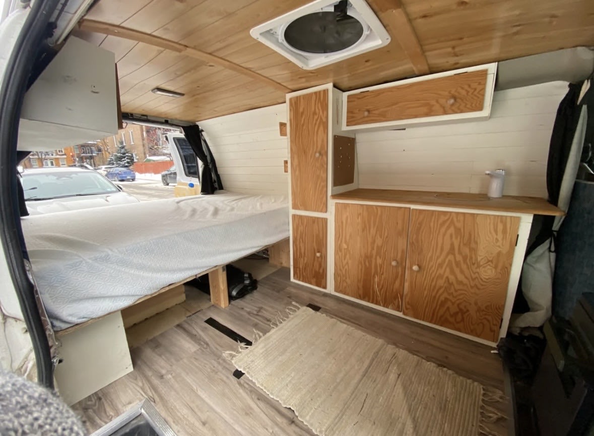 This RV rental features a cozy campervan interior with a built-in bed, wood storage cabinets, and a kitchenette.. Chevrolet Express 2500 2009