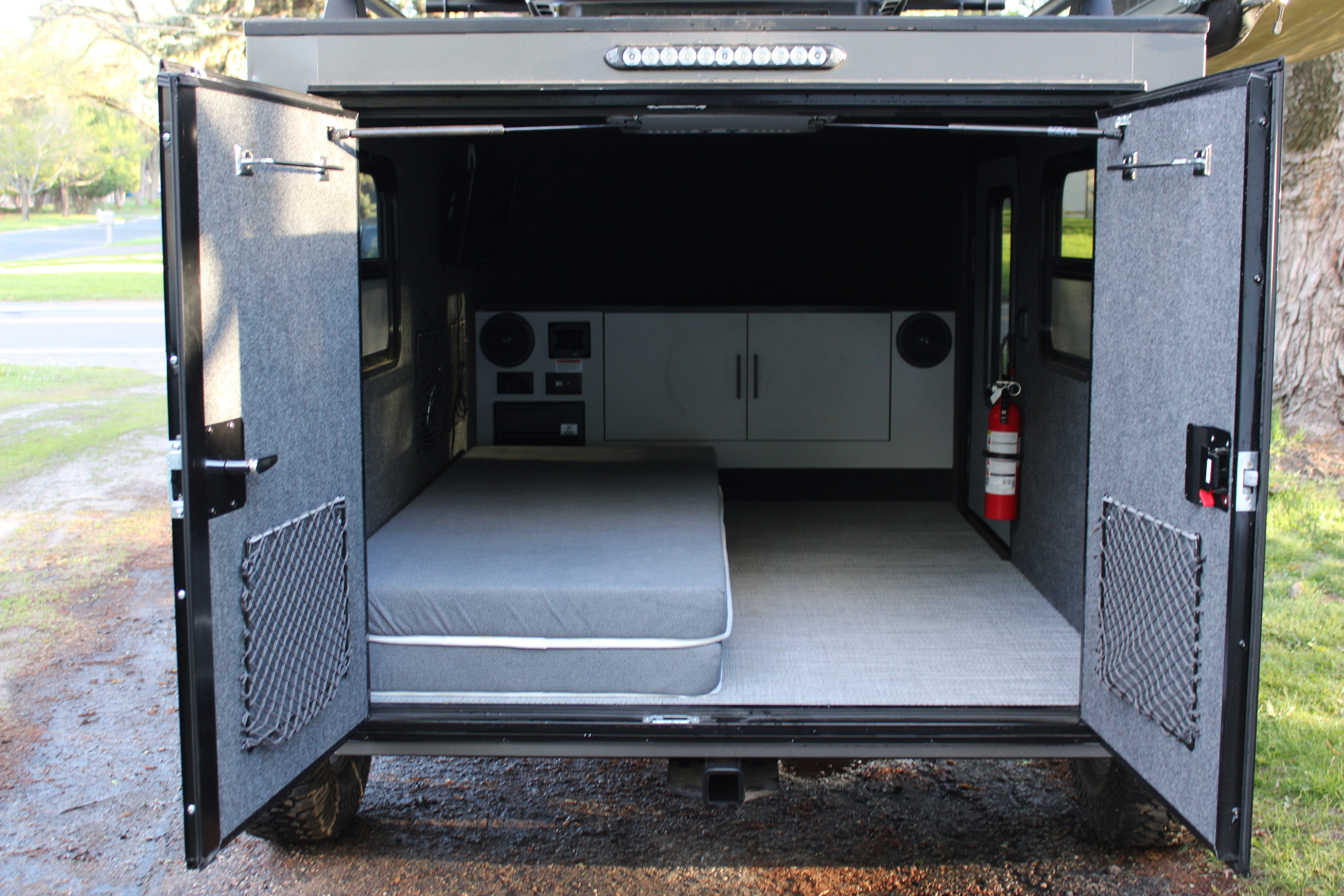 RV rental: view inside a compact camper with a bed, storage nets, controls, and a fire extinguisher ready for your adventure.. InTech RV Flyer 2023
